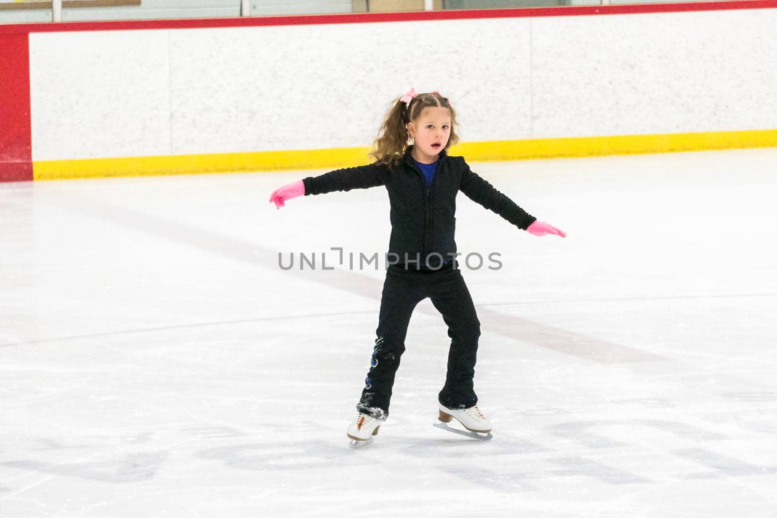 Little girl practicing figure skating moves on the indoor ice rink.