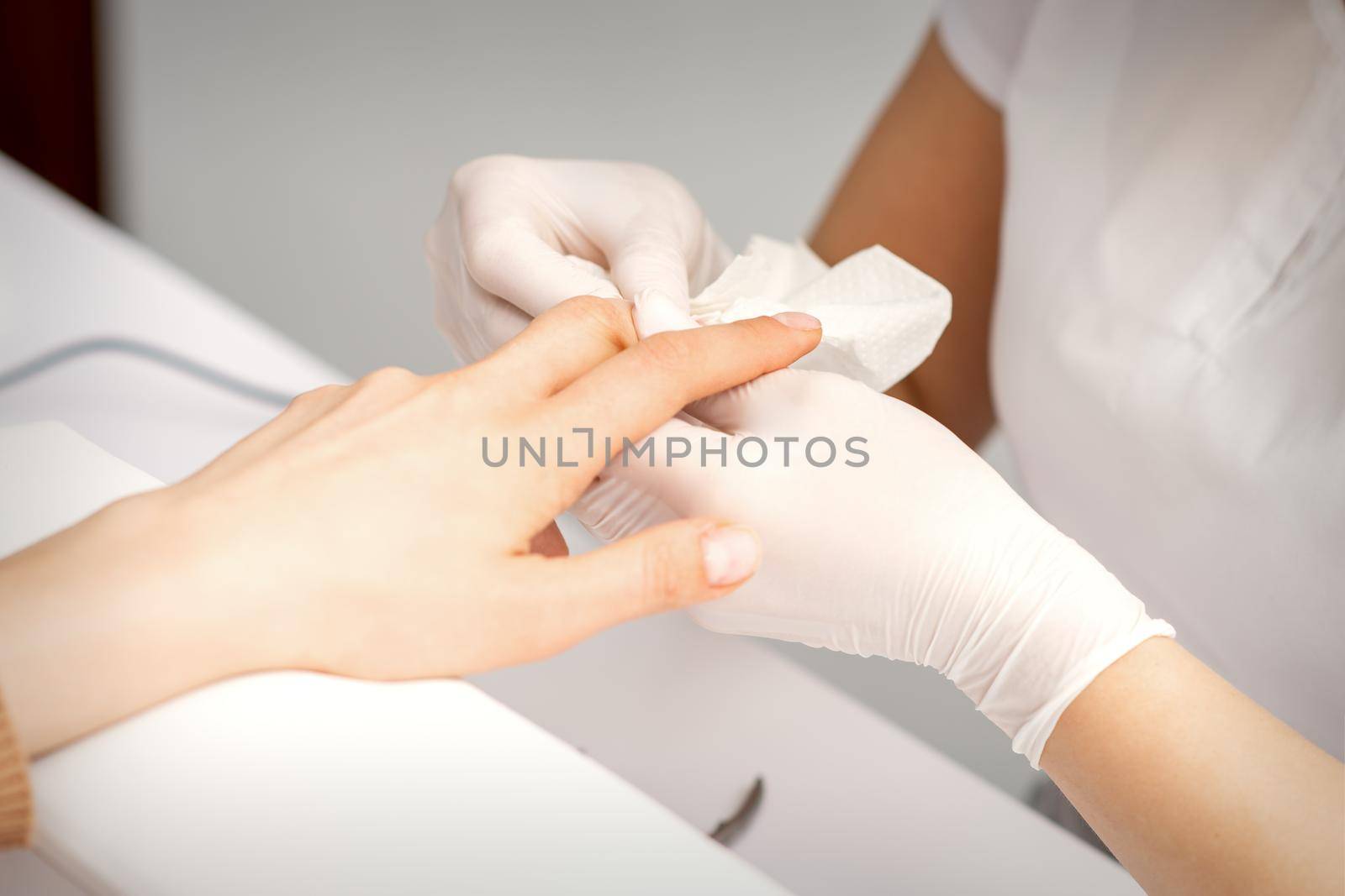 Manicure master wiping the moisturizer from the end of female fingers in beauty salon. by okskukuruza