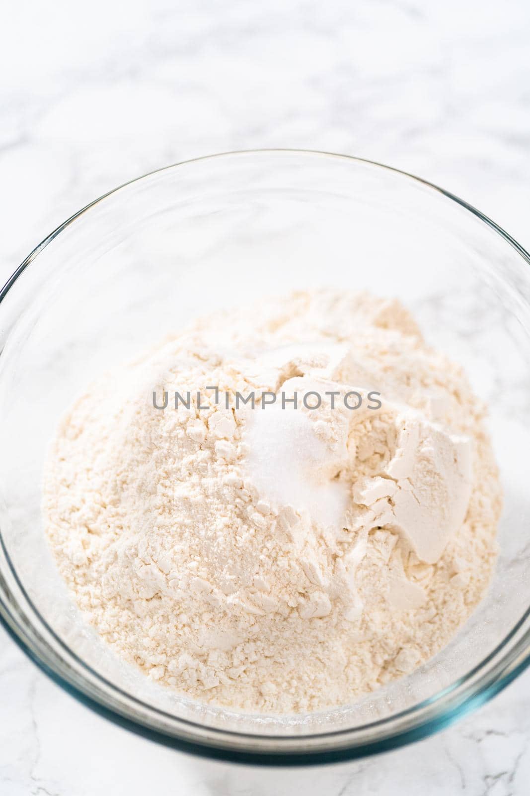 Mixing dry ingredients with a hand whisk in a large glass mixing bowl to bake mini Easter bread kulich.