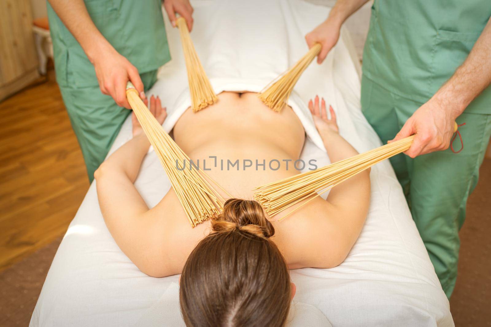 Young woman have double samurai massage with bamboo brooms in spa. Relaxation massage concept