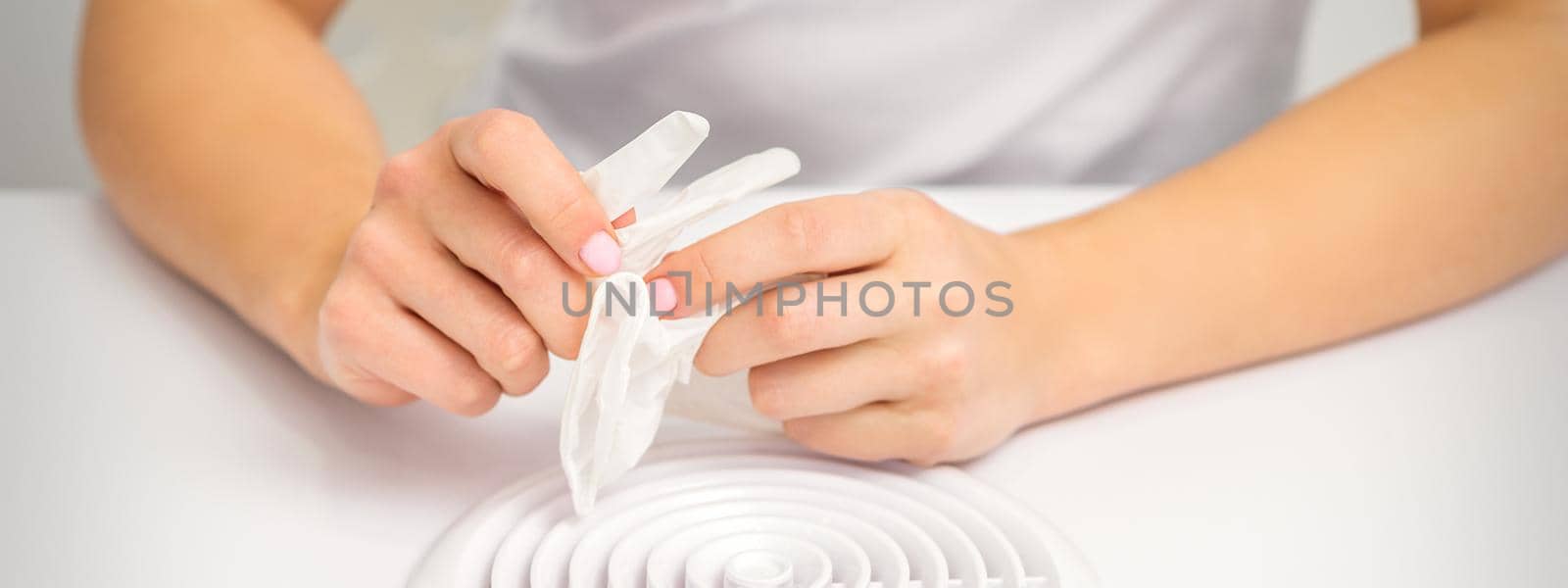 Beautician, doctor, or manicurist holds white latex protective gloves while preparing to wear them before providing services