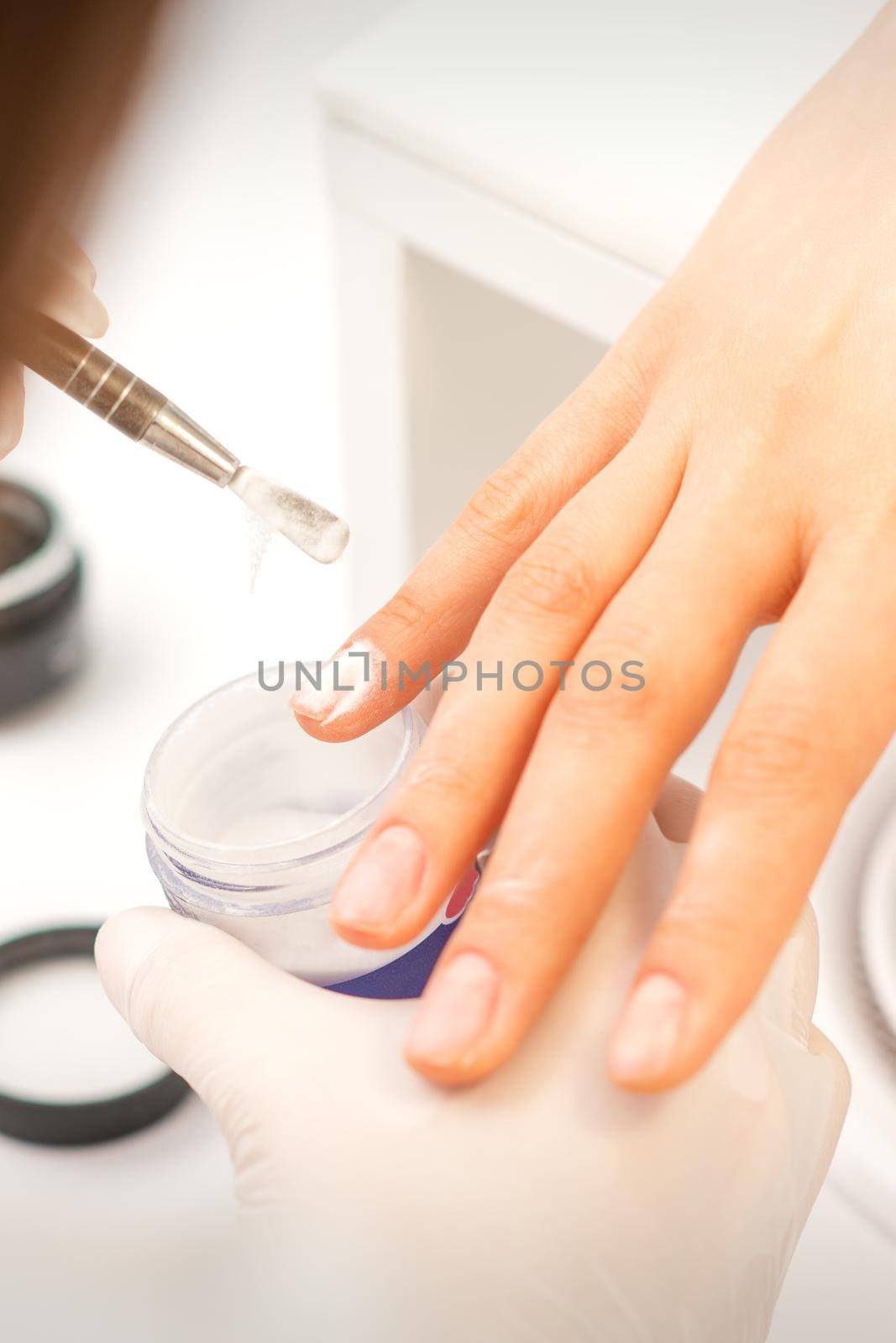 Manicure master applying acrylic powder on the female nails in a beauty salon. Strengthening of nails acrylic powder