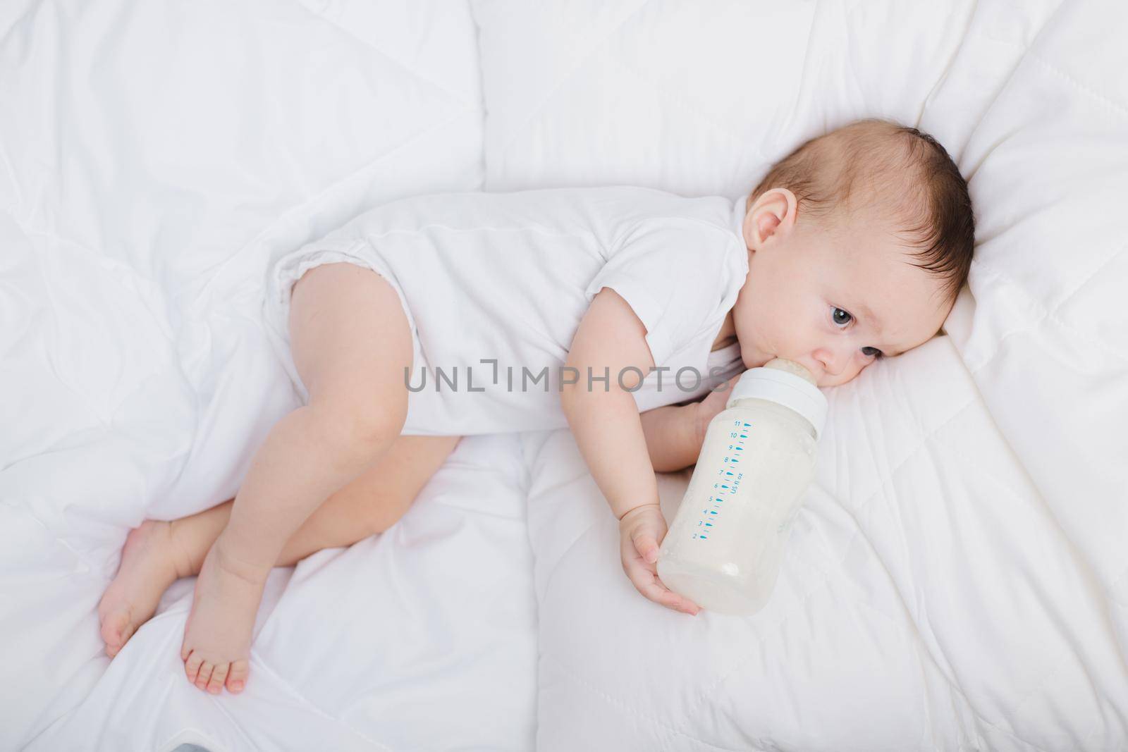 The baby in his crib eats from a bottle . Baby food copyspace . Artificial feeding. by alenka2194