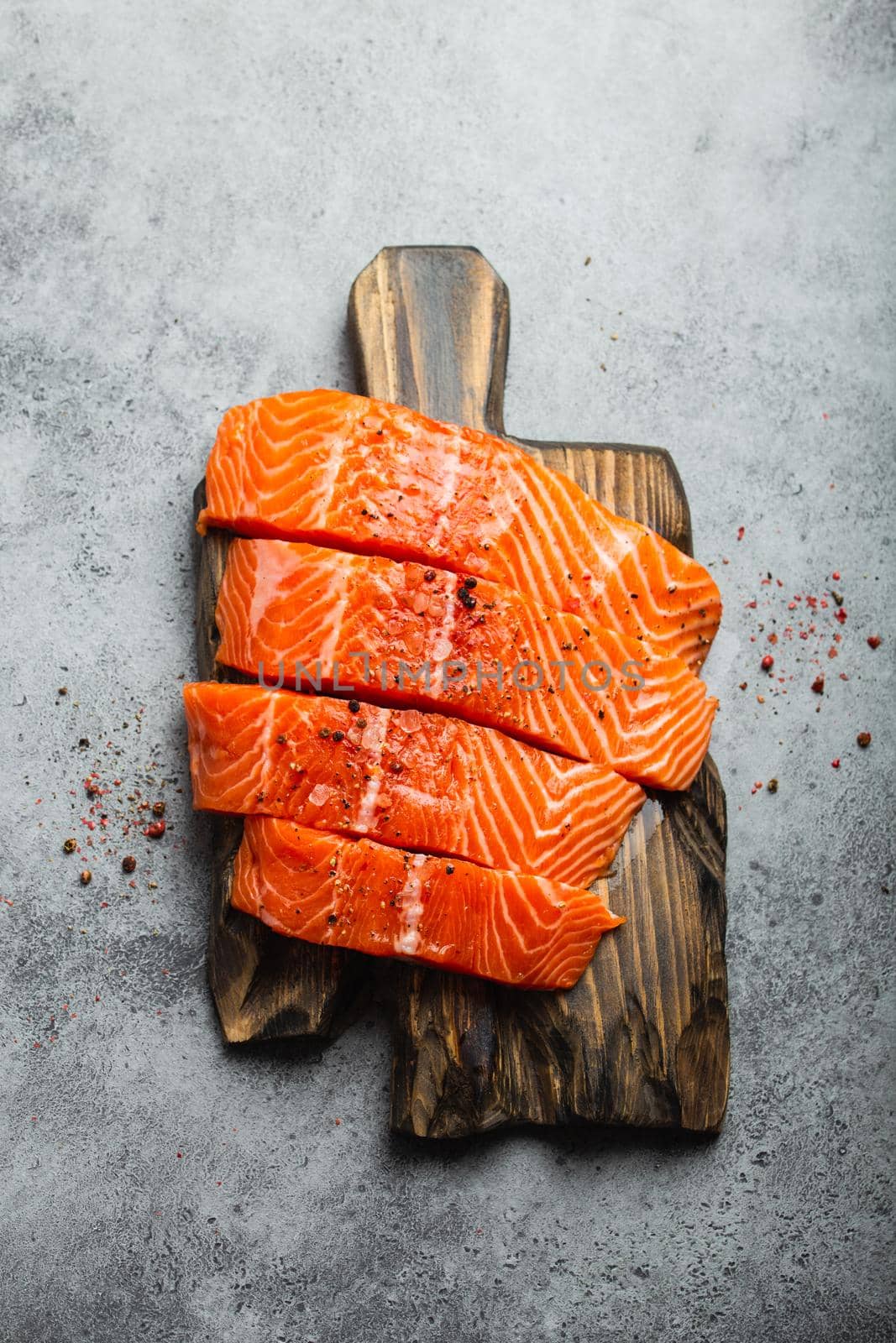 Top view, close-up of cut in slices fresh raw salmon fillet with seasonings on wooden board, gray stone background. Preparing salmon fillet for cooking, healthy eating concept
