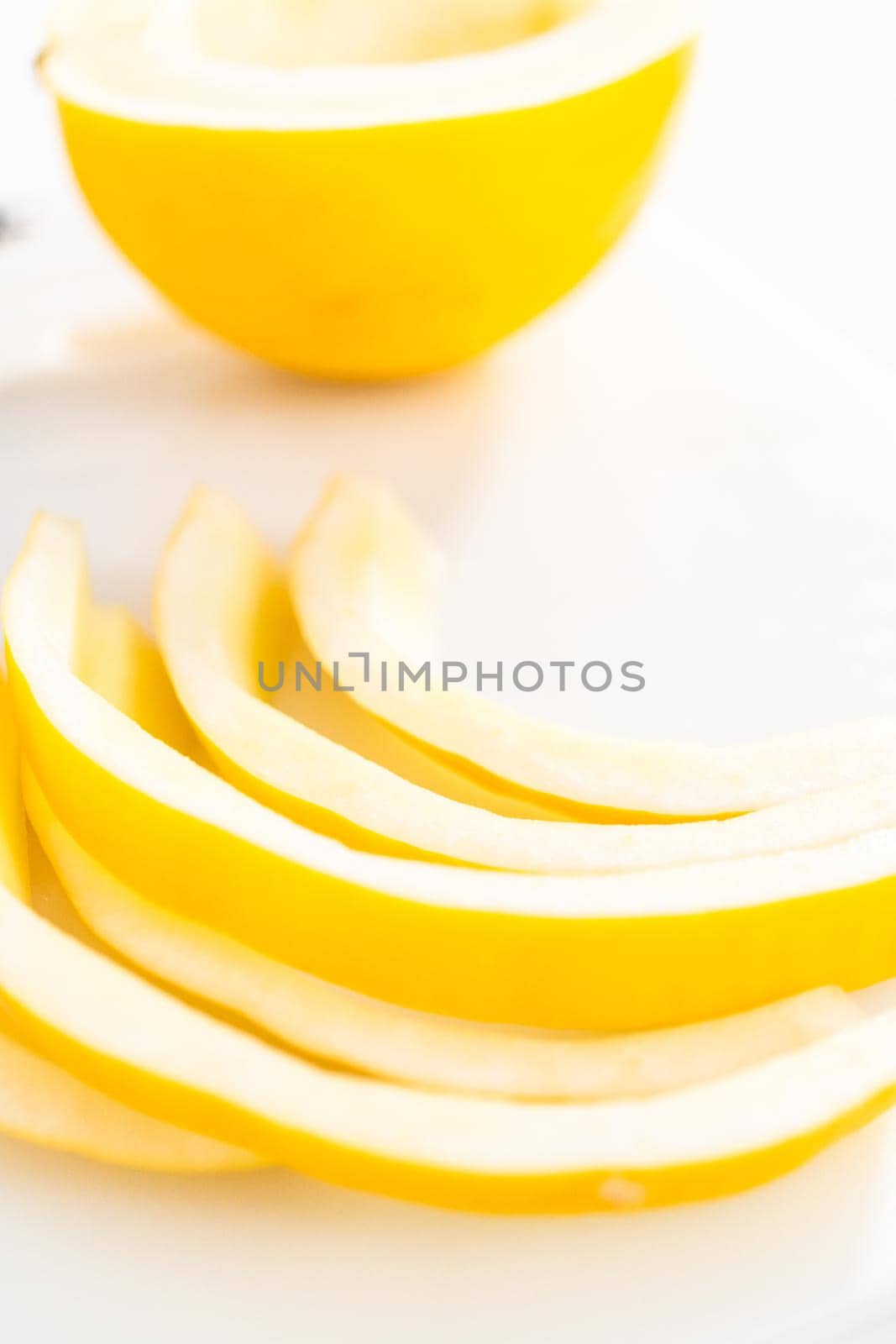 Slicong golden dewlicious melon on a white cutting board.