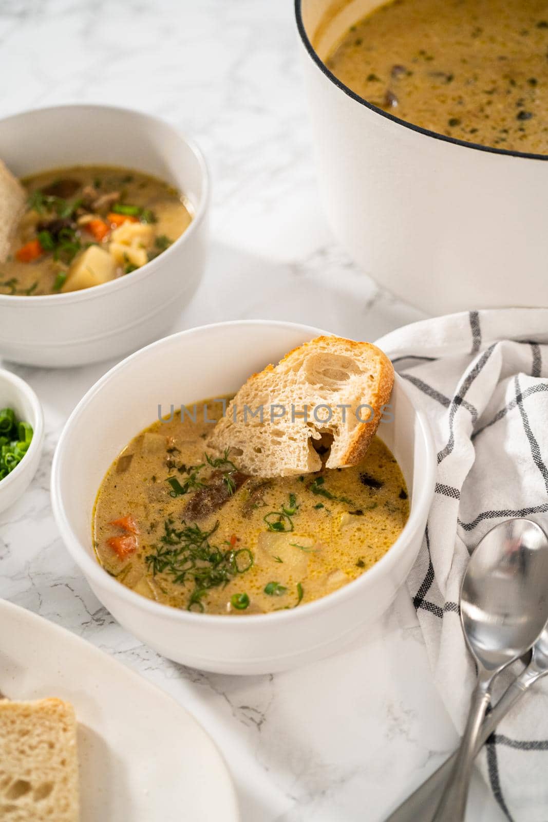 Serving creamy wild mushroom soup made out of dehydrated wild mushrooms in white bowls with sourdough bread.