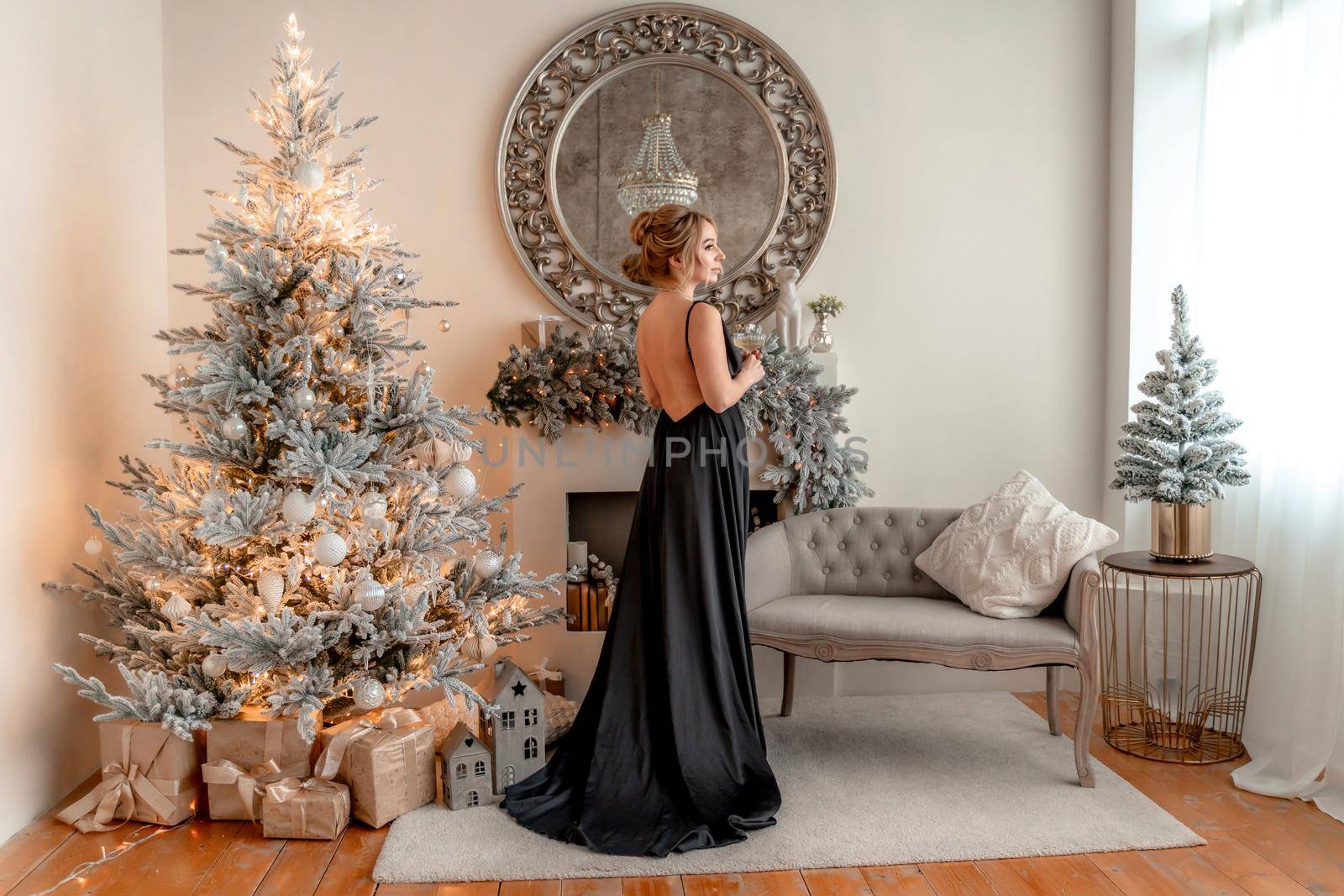 Portrait of a wealthy mature woman with evening make-up and hairstyle posing in a black dress on the background of the Christmas room. Luxurious lifestyle. Christmas holidays concept.