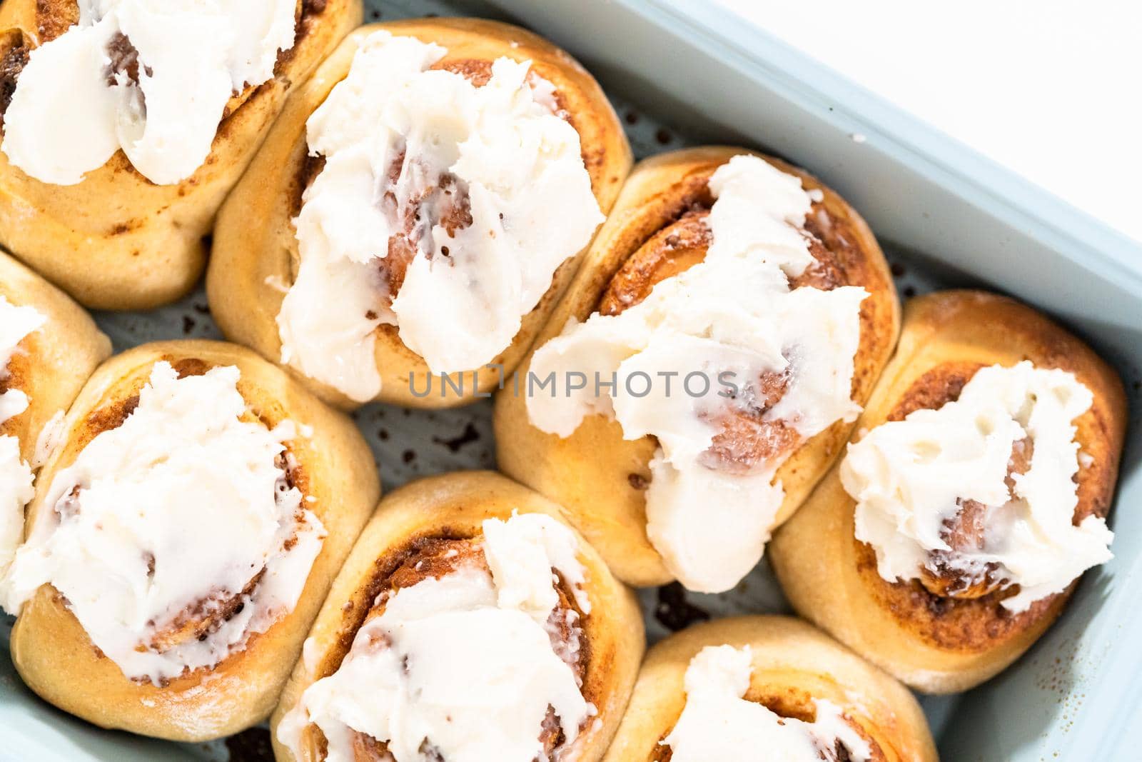 Freshly baked cinnamon rolls with white icing in a blue baking pan.