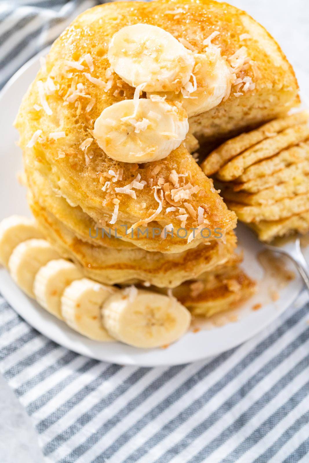 Eating freshly baked coconut banana pancakes garnished with sliced bananas and toasted coconut.