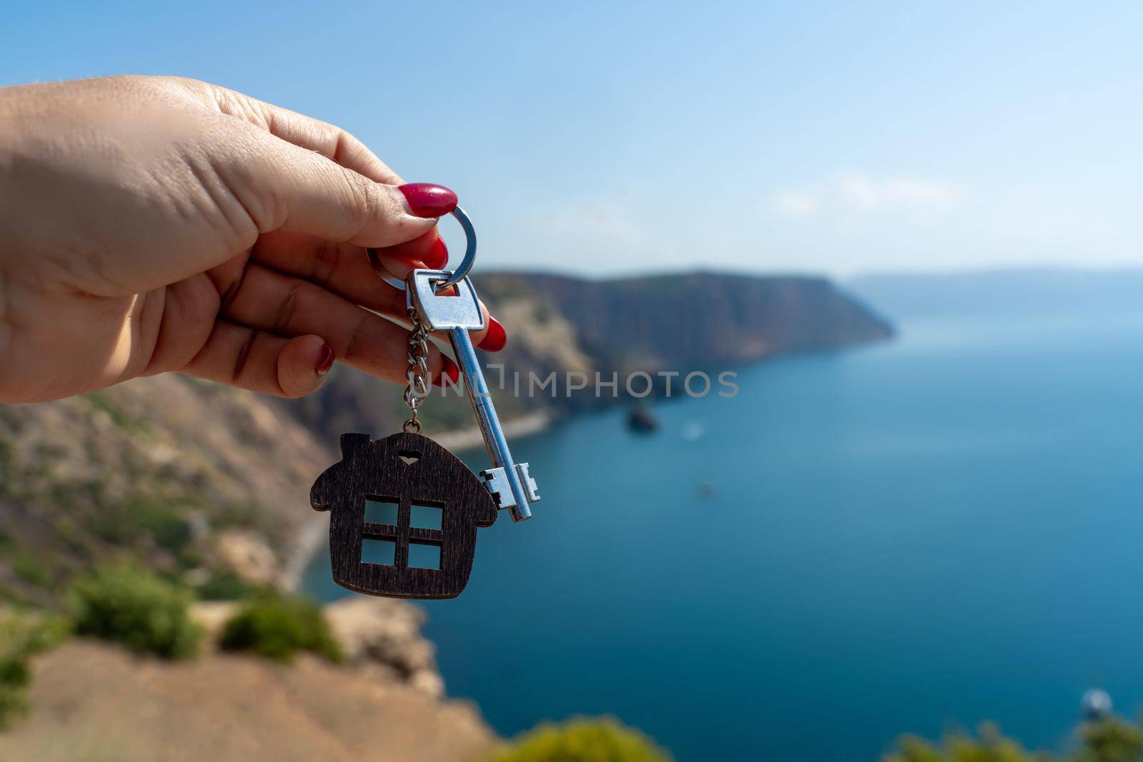 Keys with a keychain in the shape of a house in a female hand against the backdrop of the sea. The concept of buying a house, apartment, real estate, young family, mortgage loan, rental housing