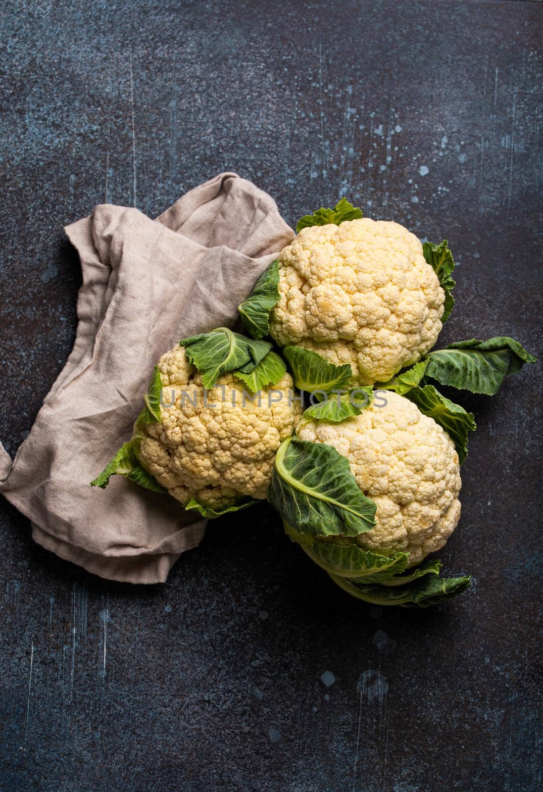 Fresh whole raw organic white cauliflower on dark stone vintage background table, ready to be cooked, top view. Vegetarian food, clean eating concept .