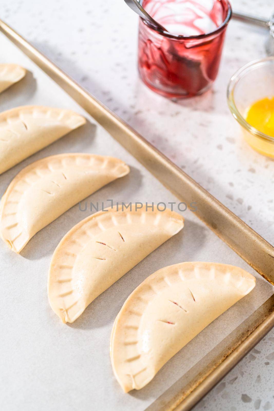 Unbaked sweet cherry empanadas on a baking sheet lined with a parchment paper baking sheet.