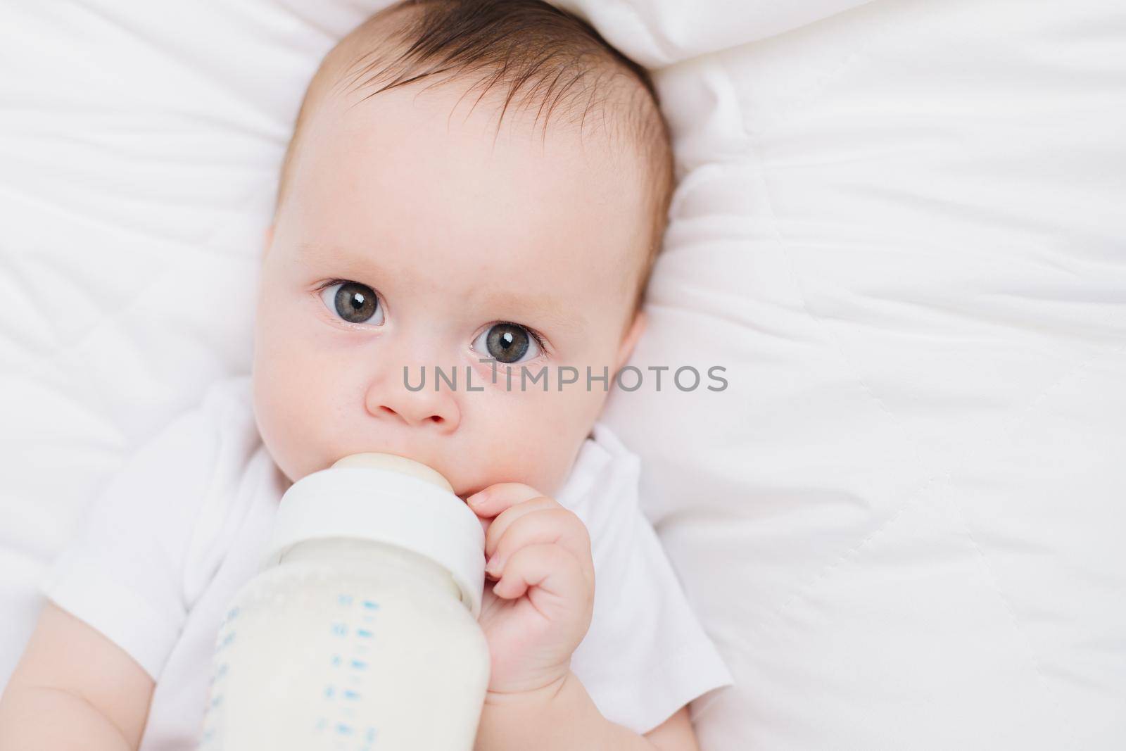 The baby in his crib eats from a bottle . Baby food copyspace . Artificial feeding. Kid top view