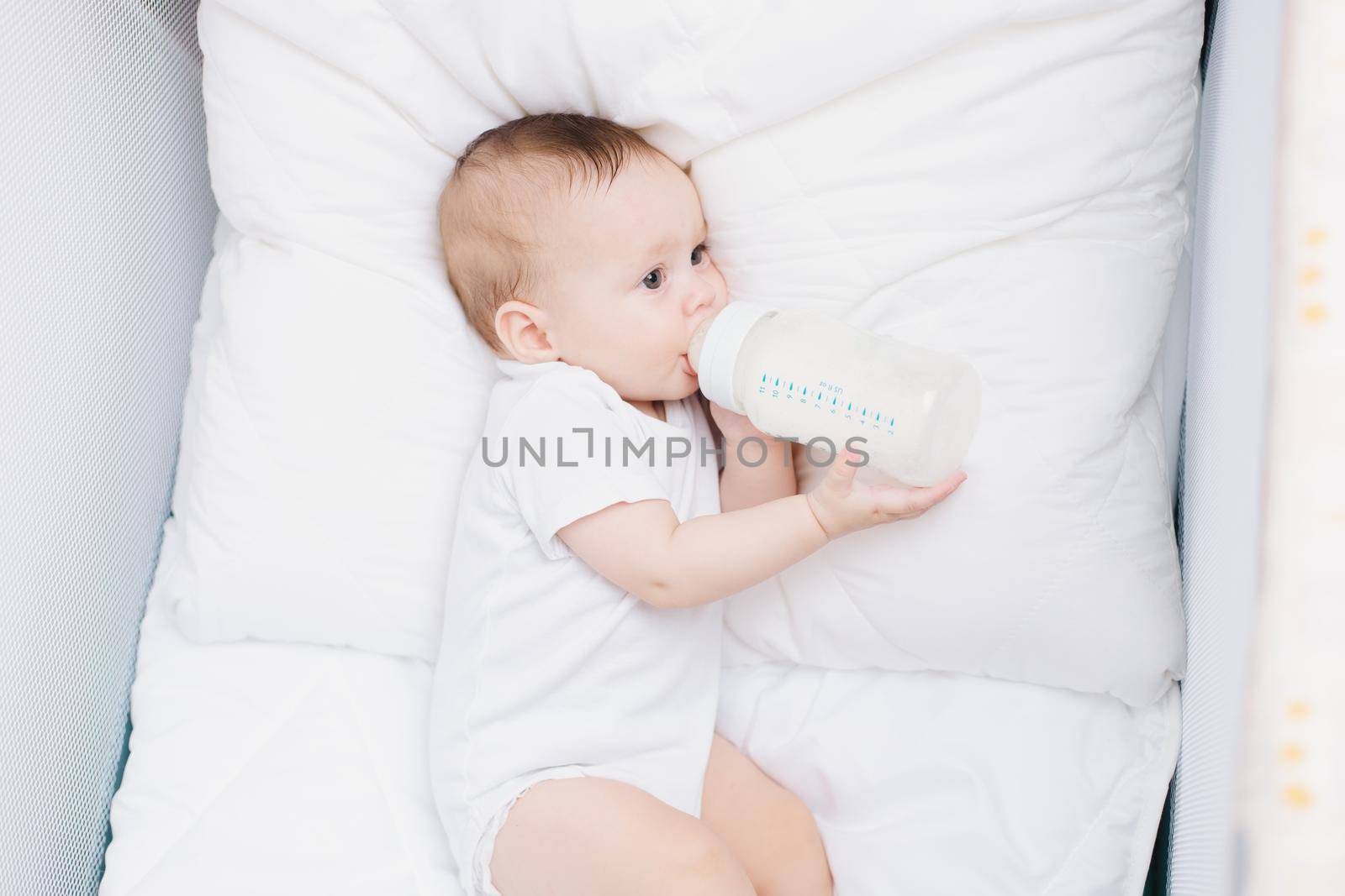 The baby in his crib eats from a bottle . Baby food copyspace . Artificial feeding. Kid top view