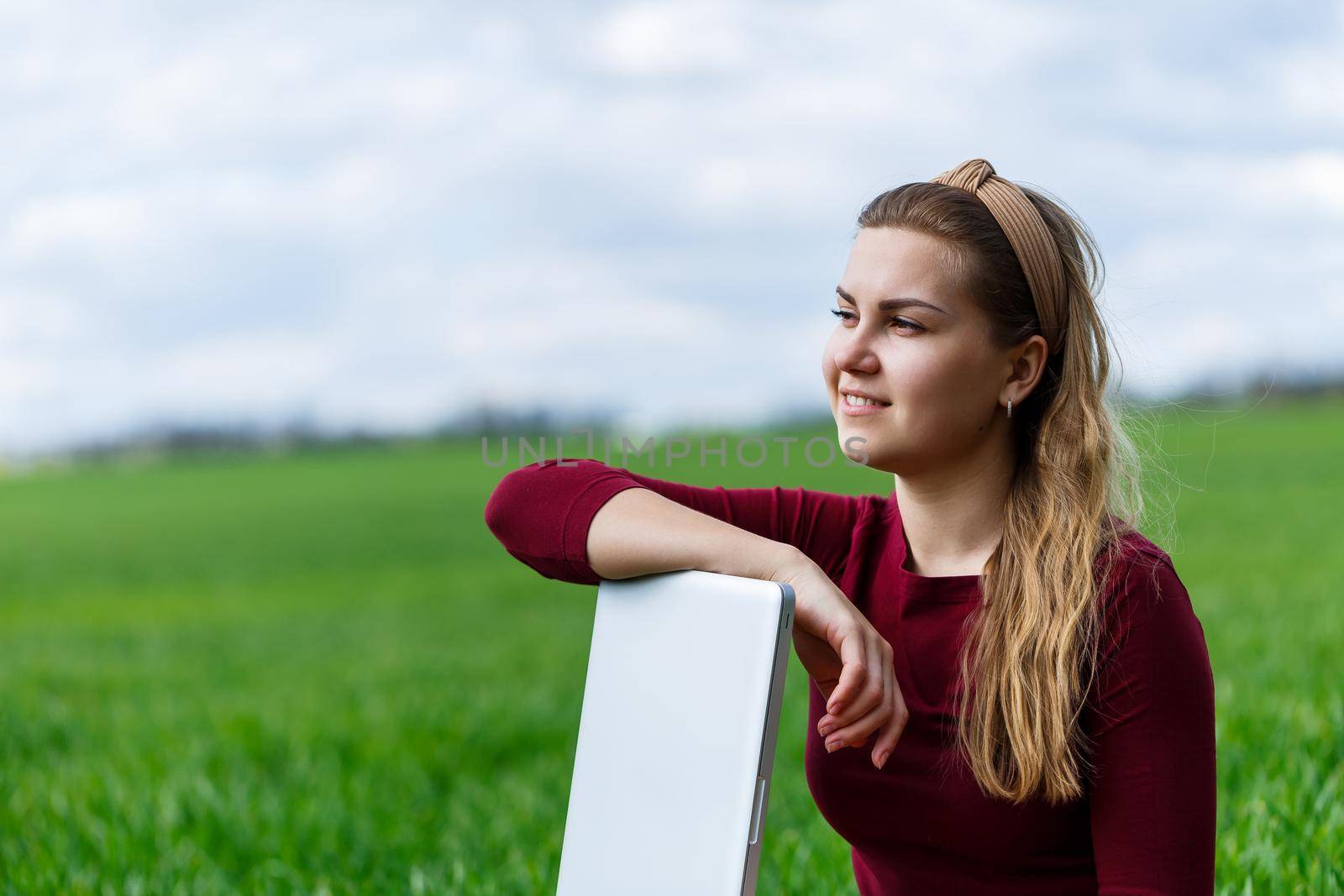 Young successful woman is sitting on green grass with a laptop in her hands. Rest after a good working day. Work on the nature. Student girl working in a secluded place. New business ideas