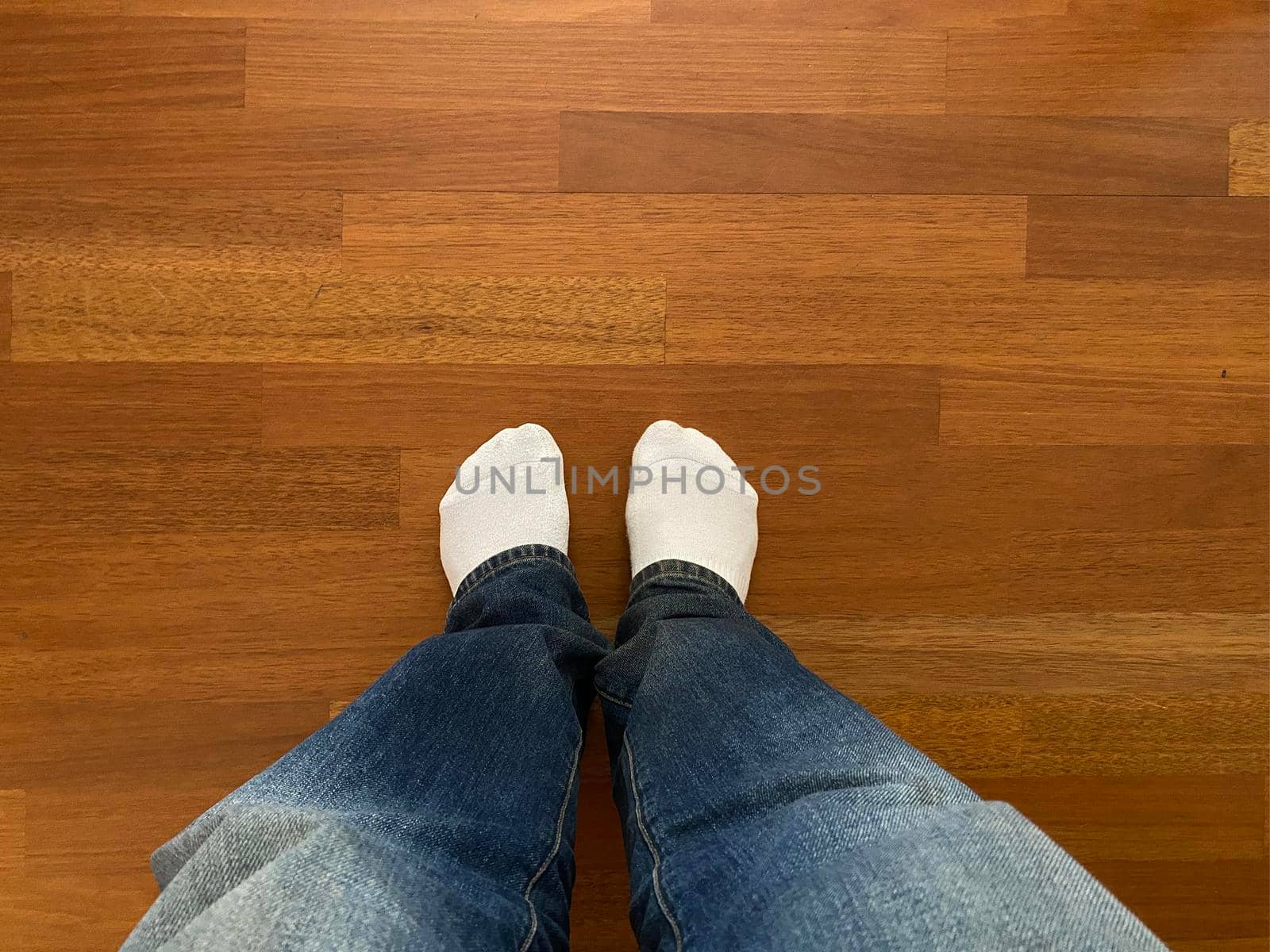 A young man legs dressed in jeans and white shocks on the wooden parquet floor background at home. Copy space.Top view by papatonic