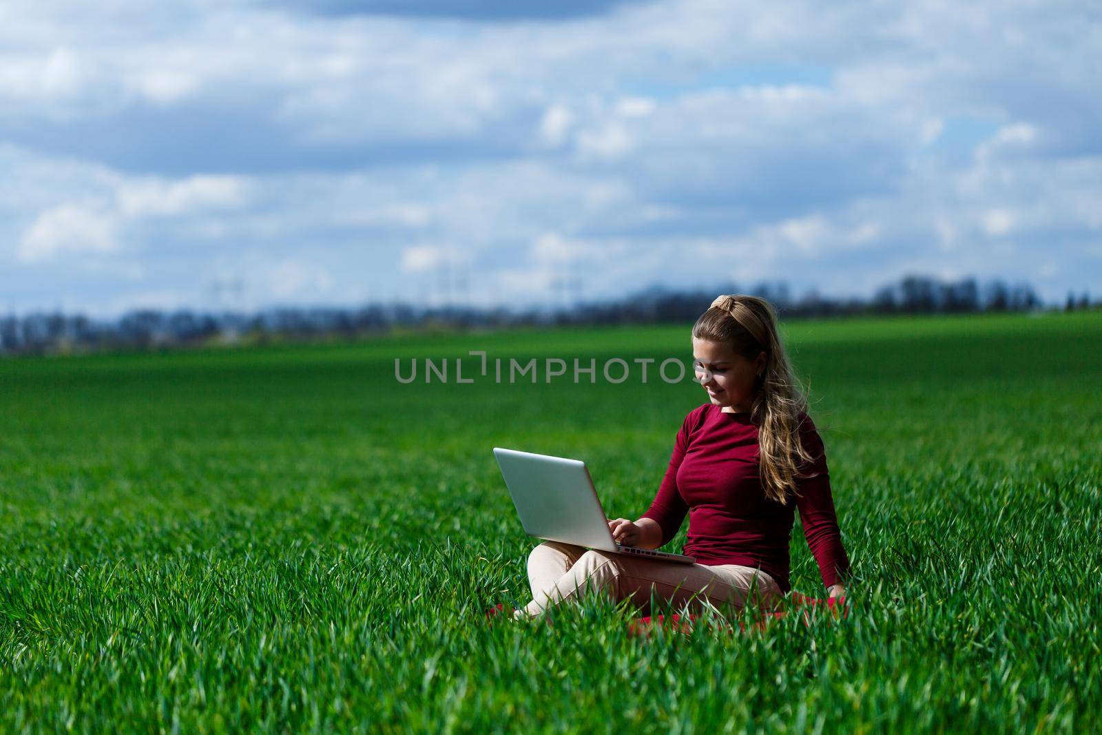 Joyful young girl on the grass with a laptop on her lap. He raised his hands up and laughed. Happiness in the lifestyle of a classical student. Work on the nature. Rest after a good working day.