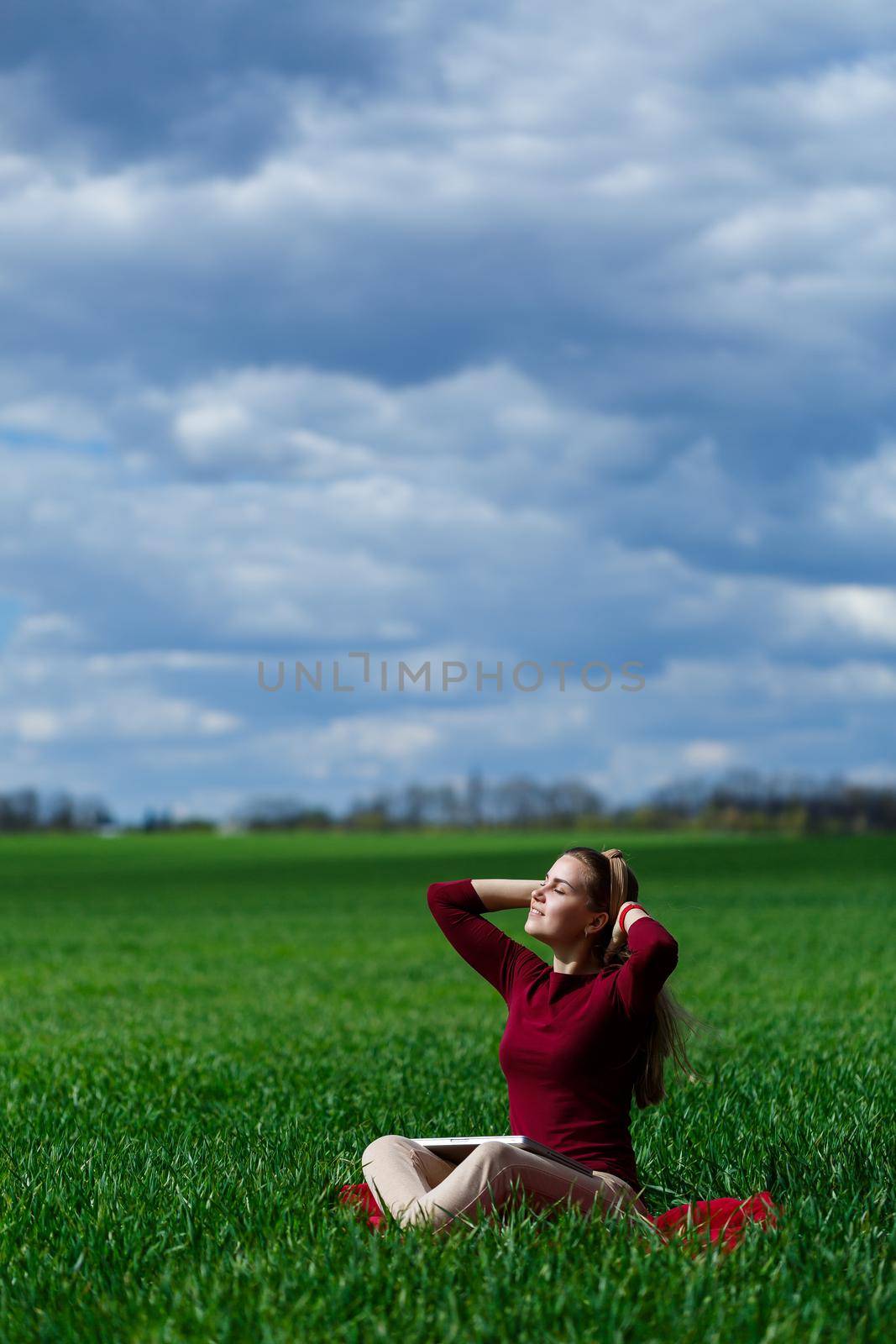 Young successful woman is sitting on green grass with a laptop in her hands. Rest after a good working day. Work on the nature. Student girl working in a secluded place. Workplace in nature