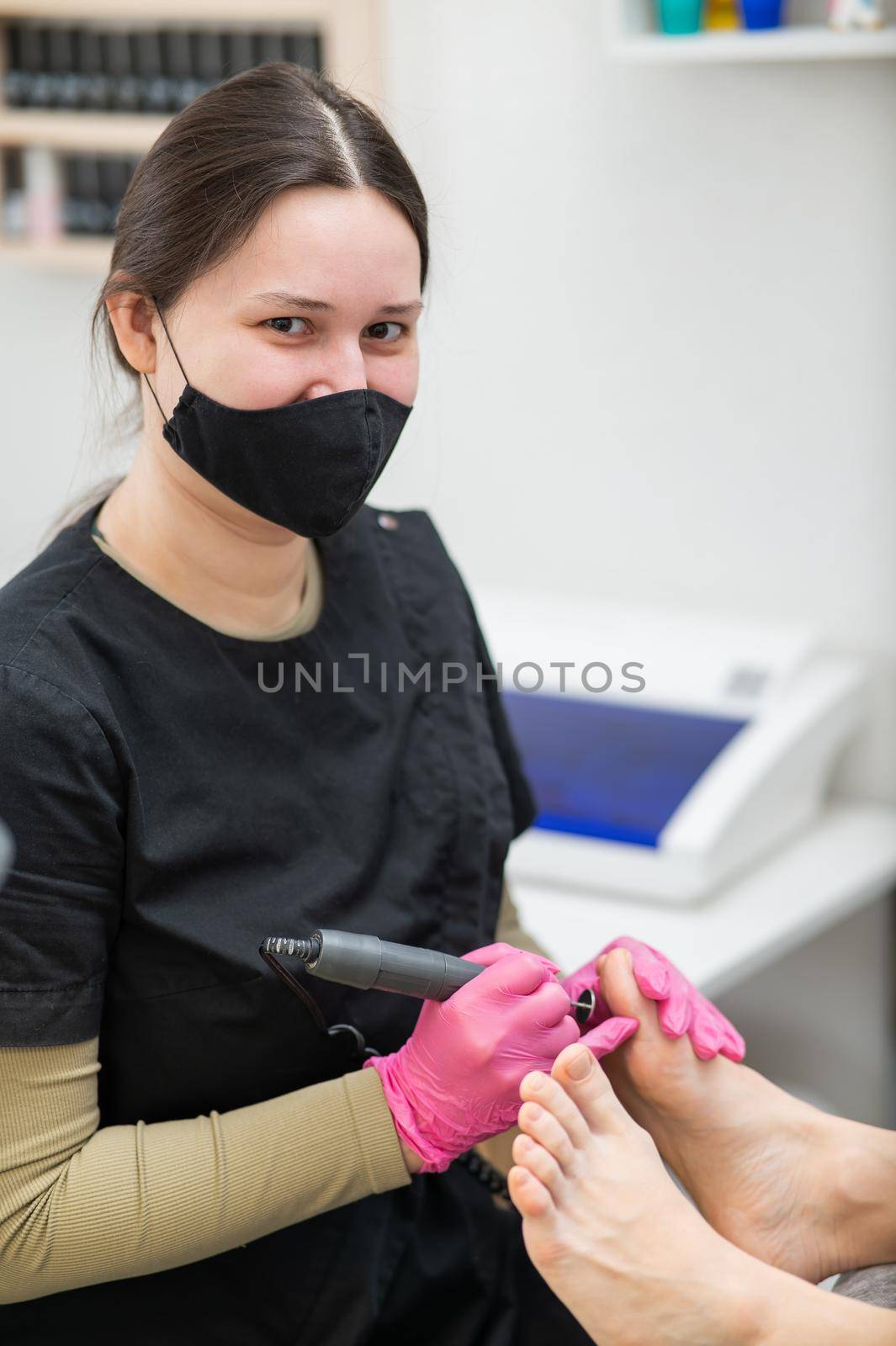 The pedicure master processes the client's foot using an apparatus with an abrasive disc
