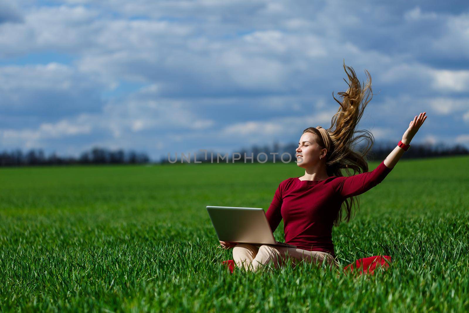 Joyful young girl on the grass with a laptop on her lap. He raised his hands up and laughed. Happiness in the lifestyle of a classical student. Work on the nature. Rest after a good working day.