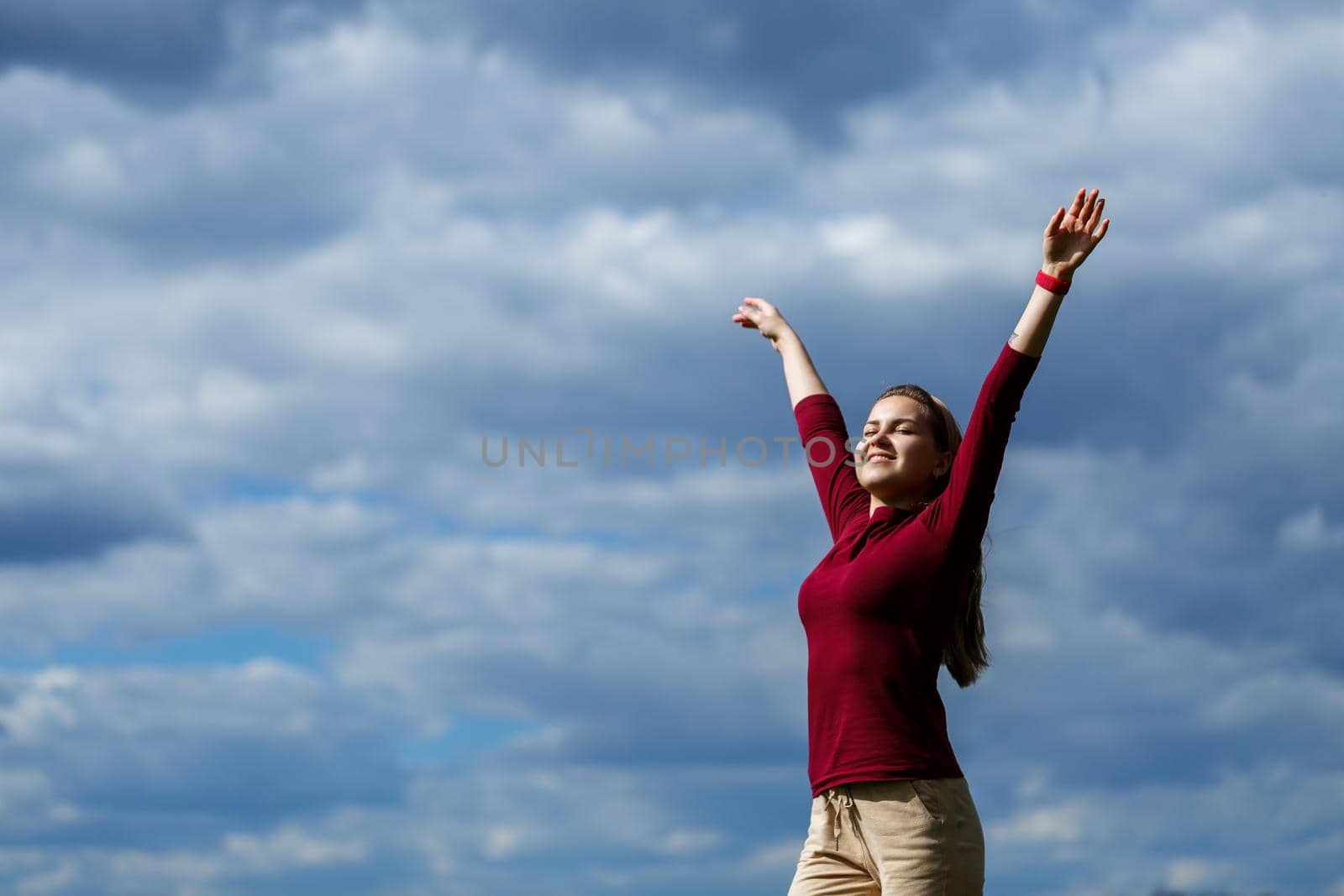 Joyful young girl on a background of the sky with clouds. He raised his hands up and laughed. Happiness in lifestyle. Inspiration in nature. Rest after a good working day.