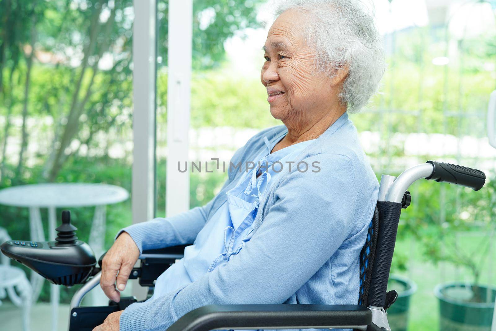 Asian elderly woman disability patient sitting on electric wheelchair in park, medical concept.