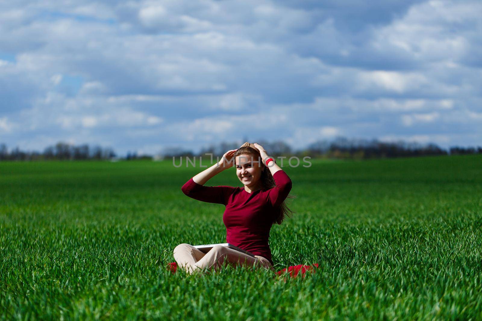 Young successful woman is sitting on green grass with a laptop in her hands. Rest after a good working day. Work on the nature. Student girl working in a secluded place. Workplace in nature by Dmitrytph