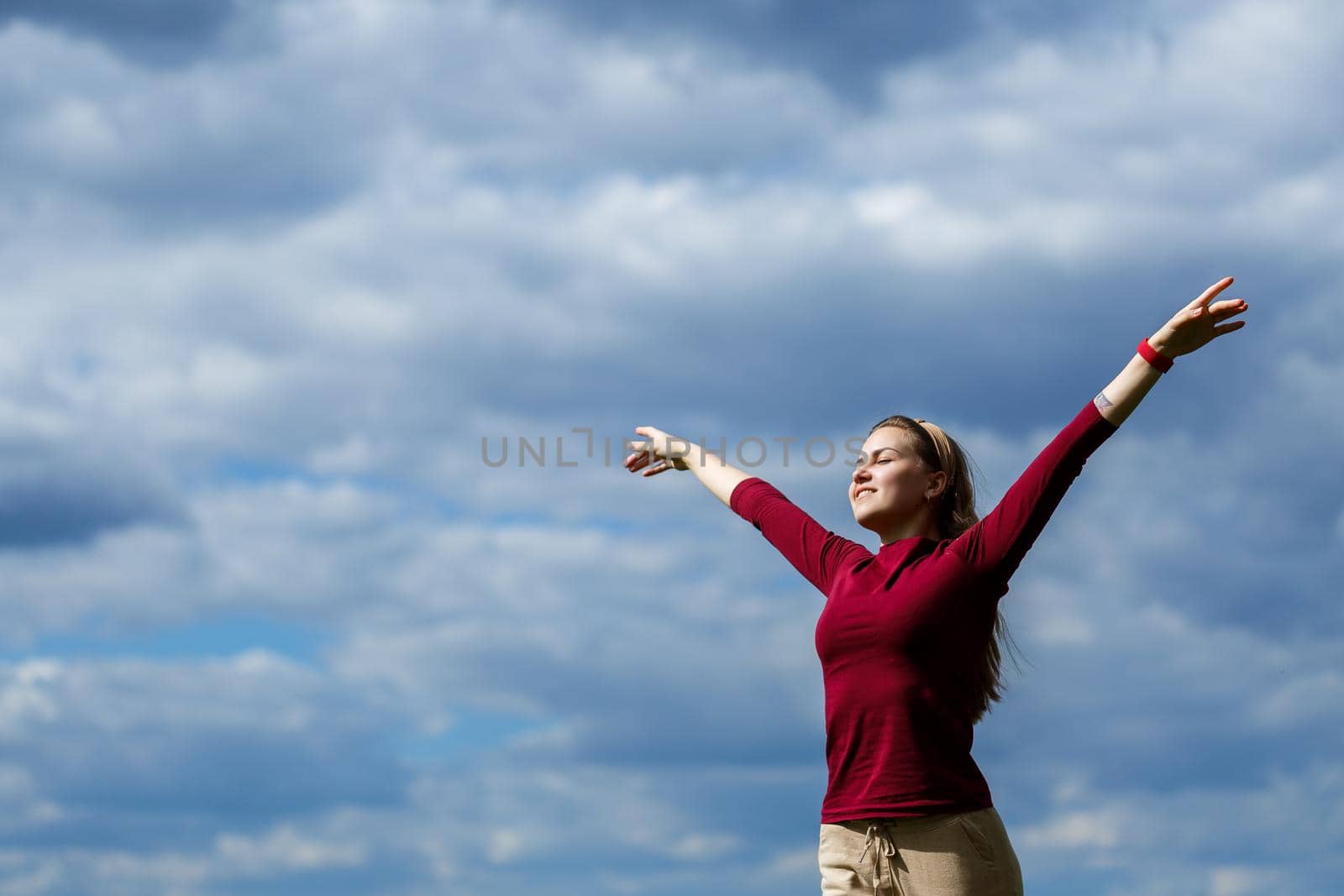 Joyful young girl on a background of the sky with clouds. He raised his hands up and laughed. Happiness in lifestyle. Inspiration in nature. Rest after a good working day.