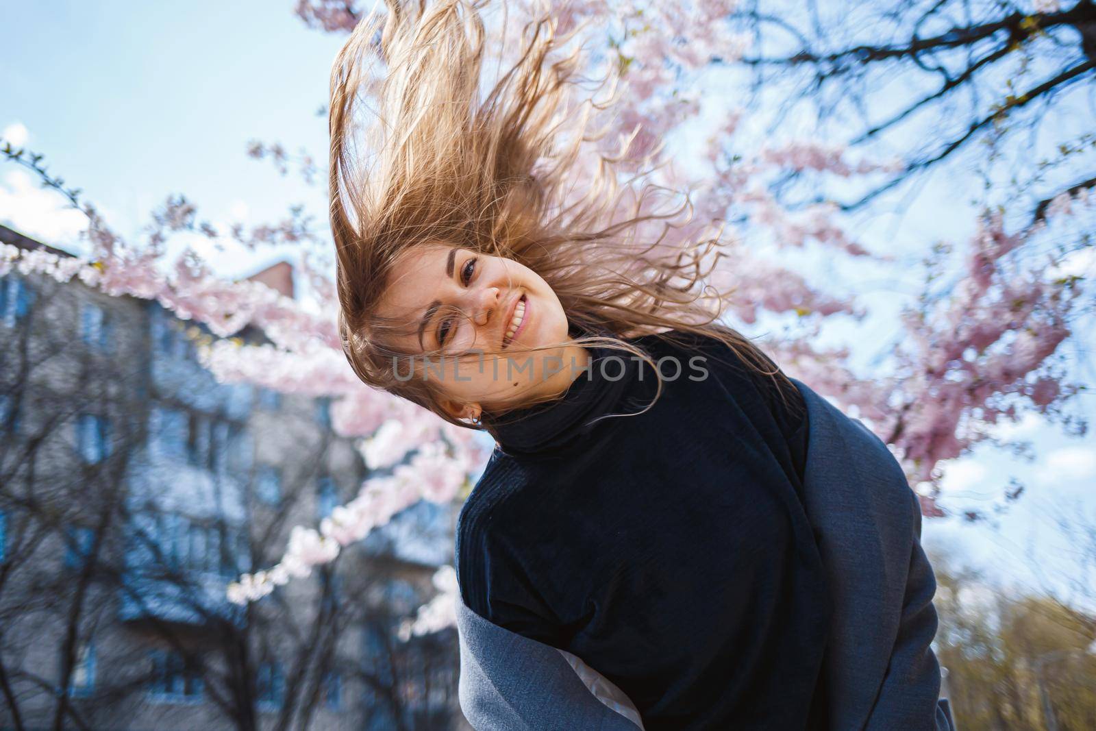 Sakura branches with flowers on a tree on the city streets. Happy woman girl spinning on the street with blooming sakura. Gorgeous fashionable girl outdoors. Sakura tree blossoms.
