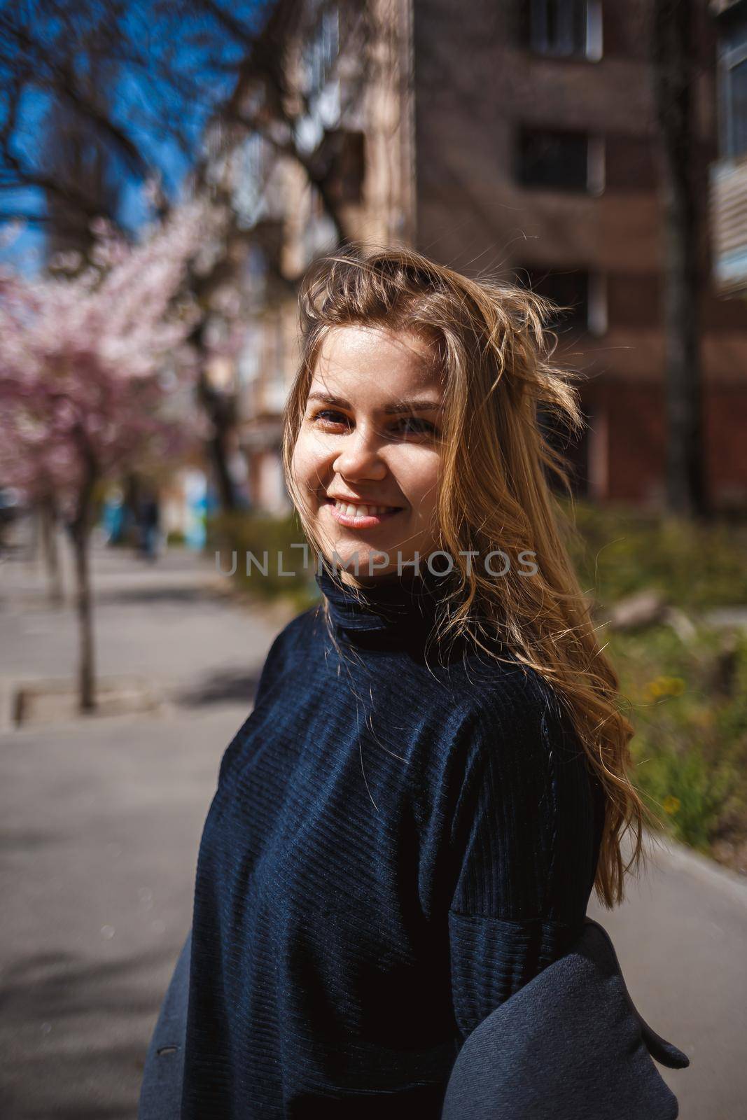 Sakura branches with flowers on a tree on the city streets. Happy woman girl spinning on the street with blooming sakura. Gorgeous fashionable girl outdoors. Sakura tree blossoms.
