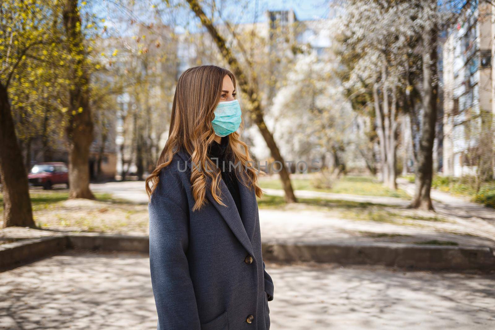 Girl, young woman in a protective sterile medical mask on her face, looking at the camera outdoors, in the spring garden. Air pollution, virus, pandemic coronavirus concept.