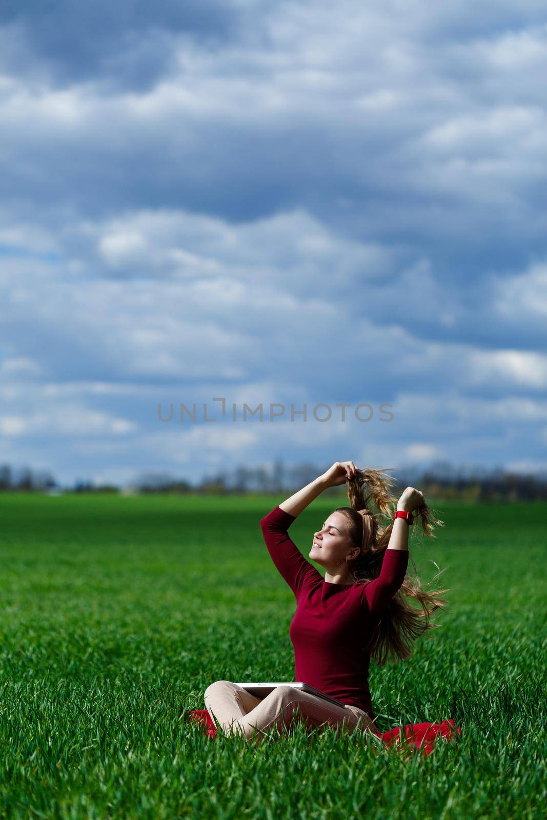 Young successful woman is sitting on green grass with a laptop in her hands. Rest after a good working day. Work on the nature. Student girl working in a secluded place. Workplace in nature