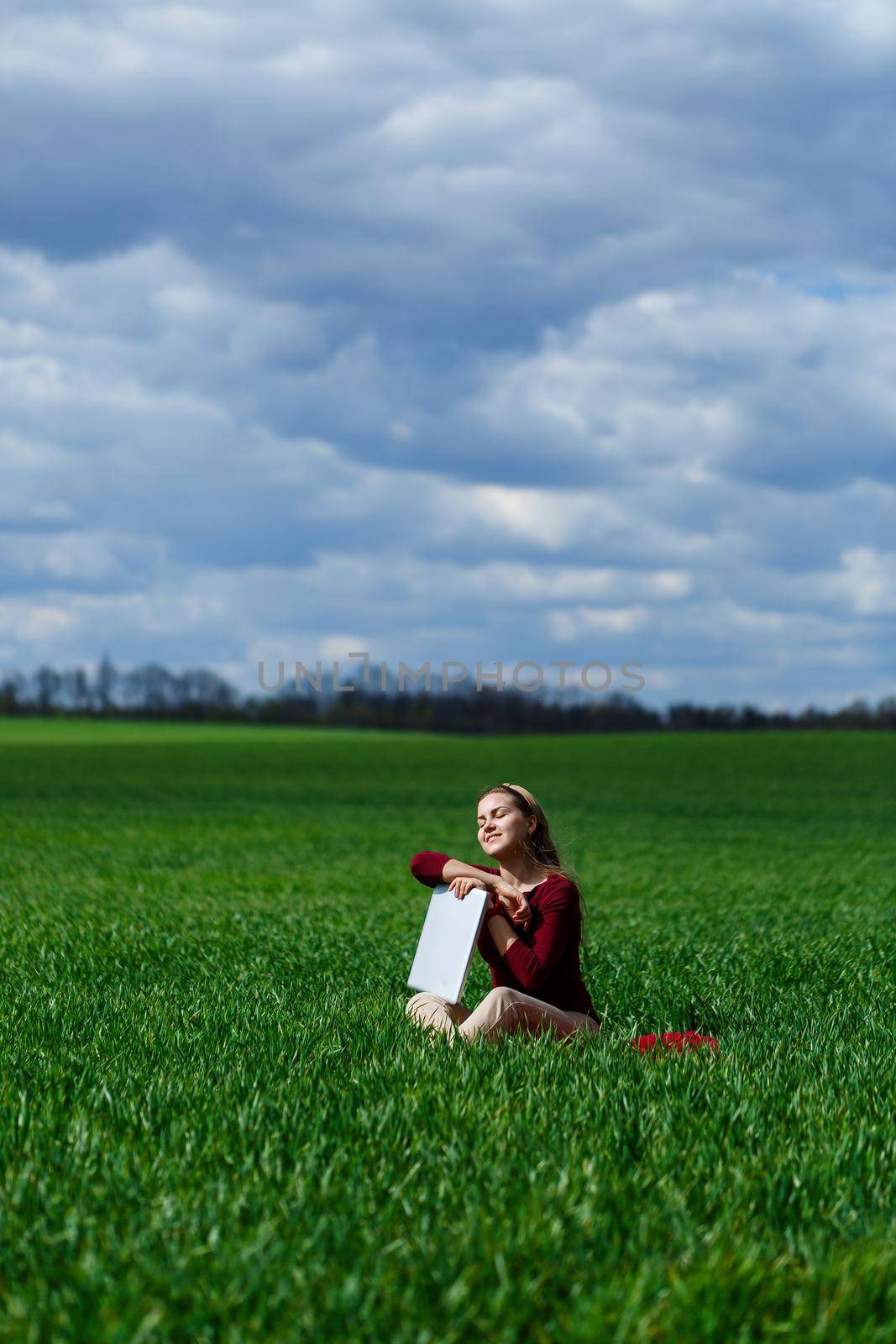 Young successful woman is sitting on green grass with a laptop in her hands. Rest after a good working day. Work on the nature. Student girl working in a secluded place. Workplace in nature