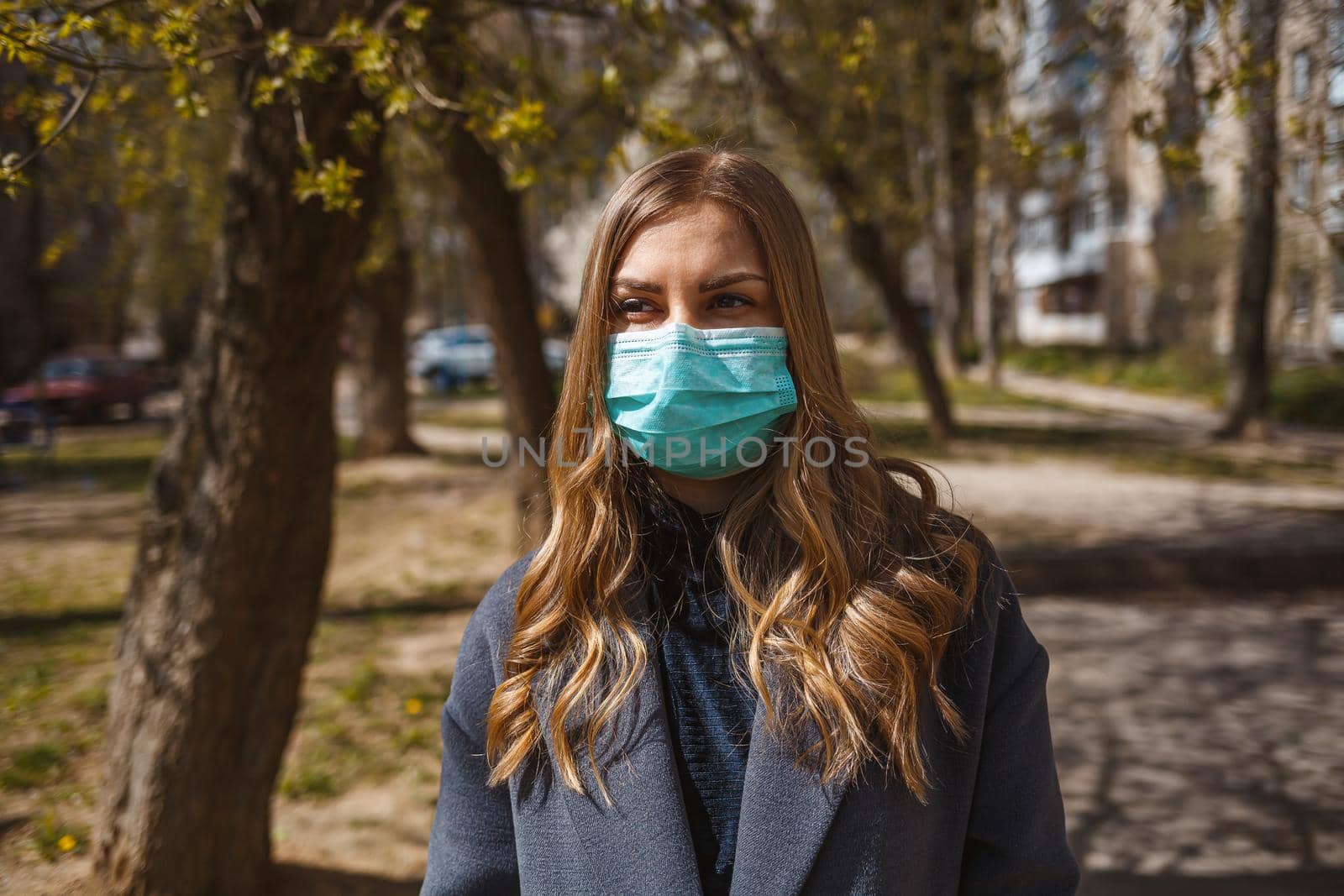 Girl, young woman in a protective sterile medical mask on her face, looking at the camera outdoors, in the spring garden. Air pollution, virus, pandemic coronavirus concept.