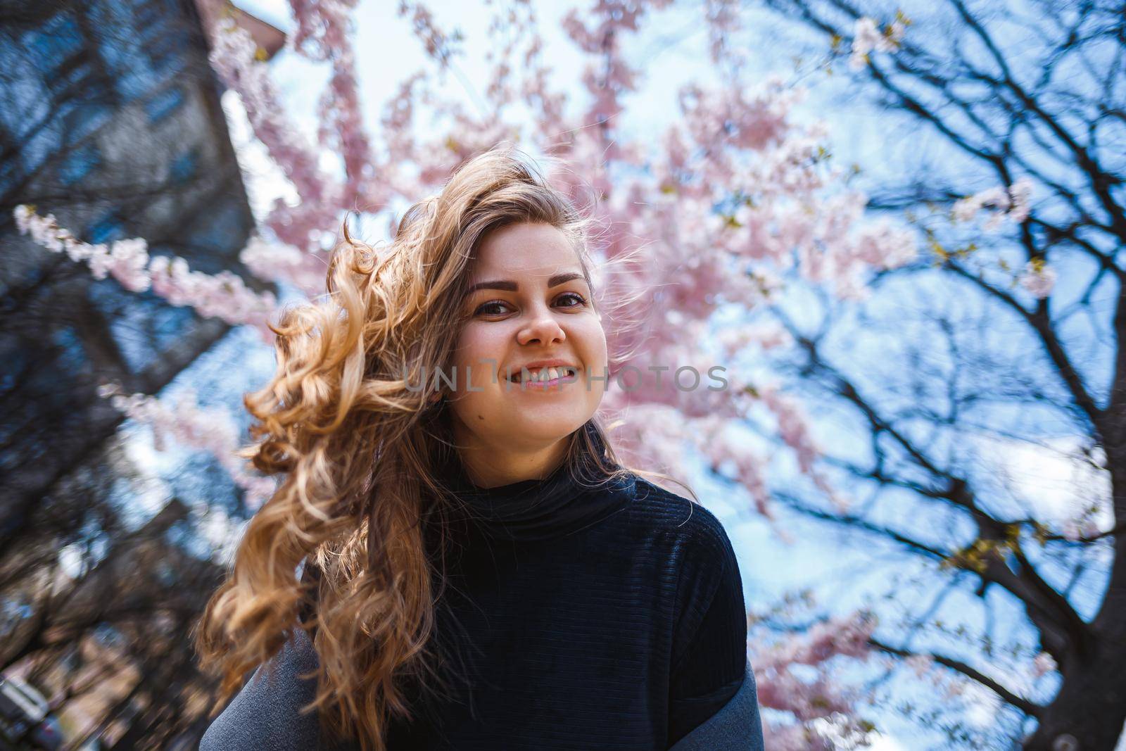 Sakura branches with flowers on a tree on the city streets. Happy woman girl spinning on the street with blooming sakura. Gorgeous fashionable girl outdoors. Sakura tree blossoms.