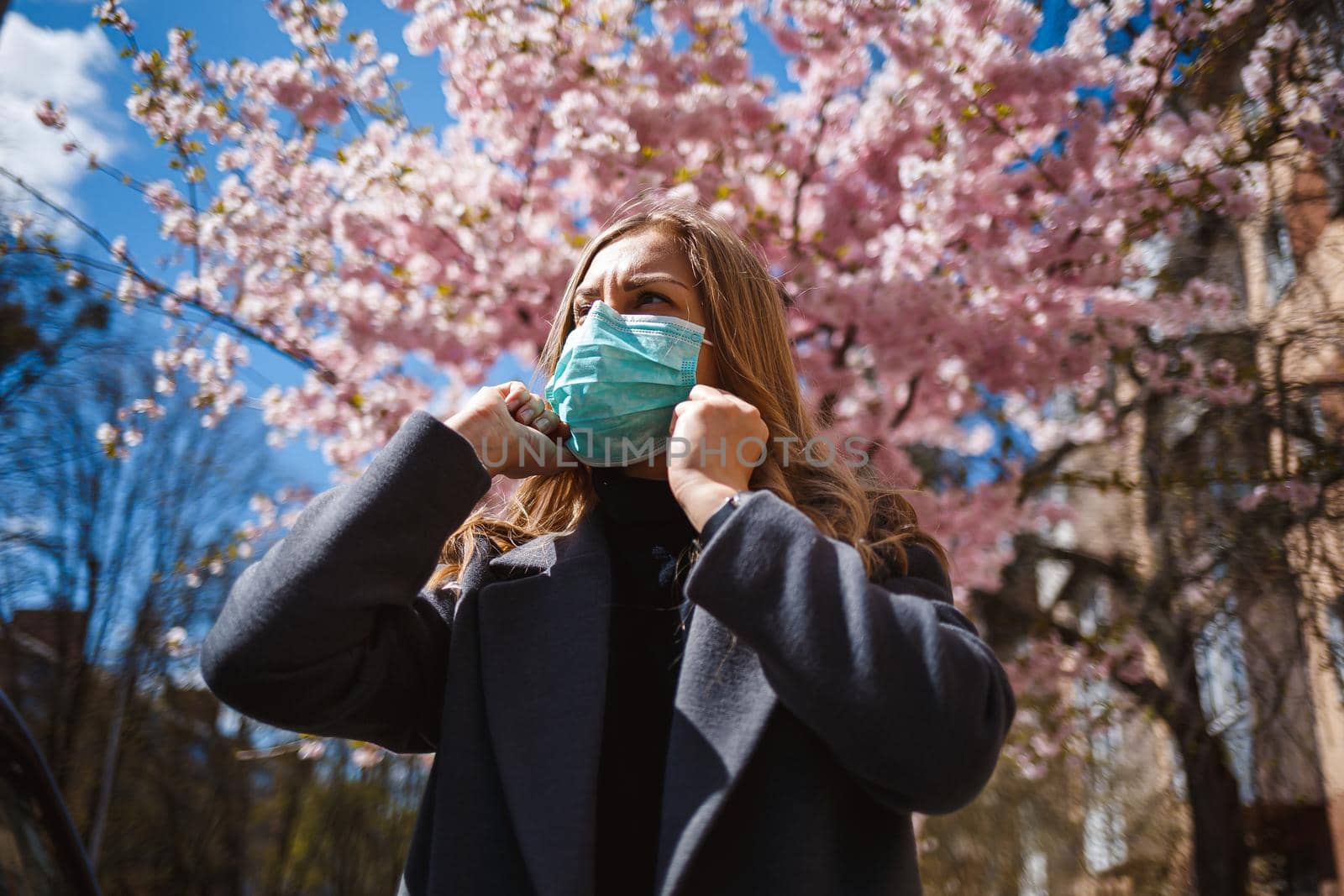 Girl, young woman in a protective sterile medical mask on her face, looking at the camera outdoors, in the spring garden. Air pollution, virus, pandemic coronavirus concept.