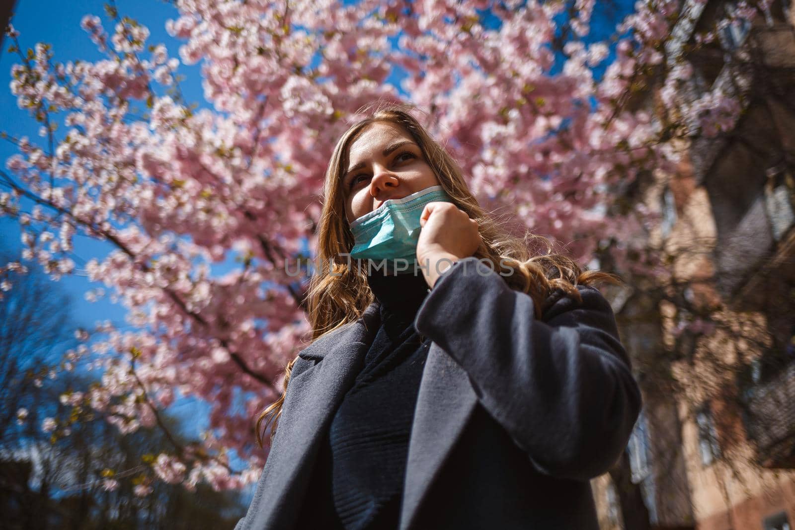 Girl, young woman in a protective sterile medical mask on her face, looking at the camera outdoors, in the spring garden. Air pollution, virus, pandemic coronavirus concept.