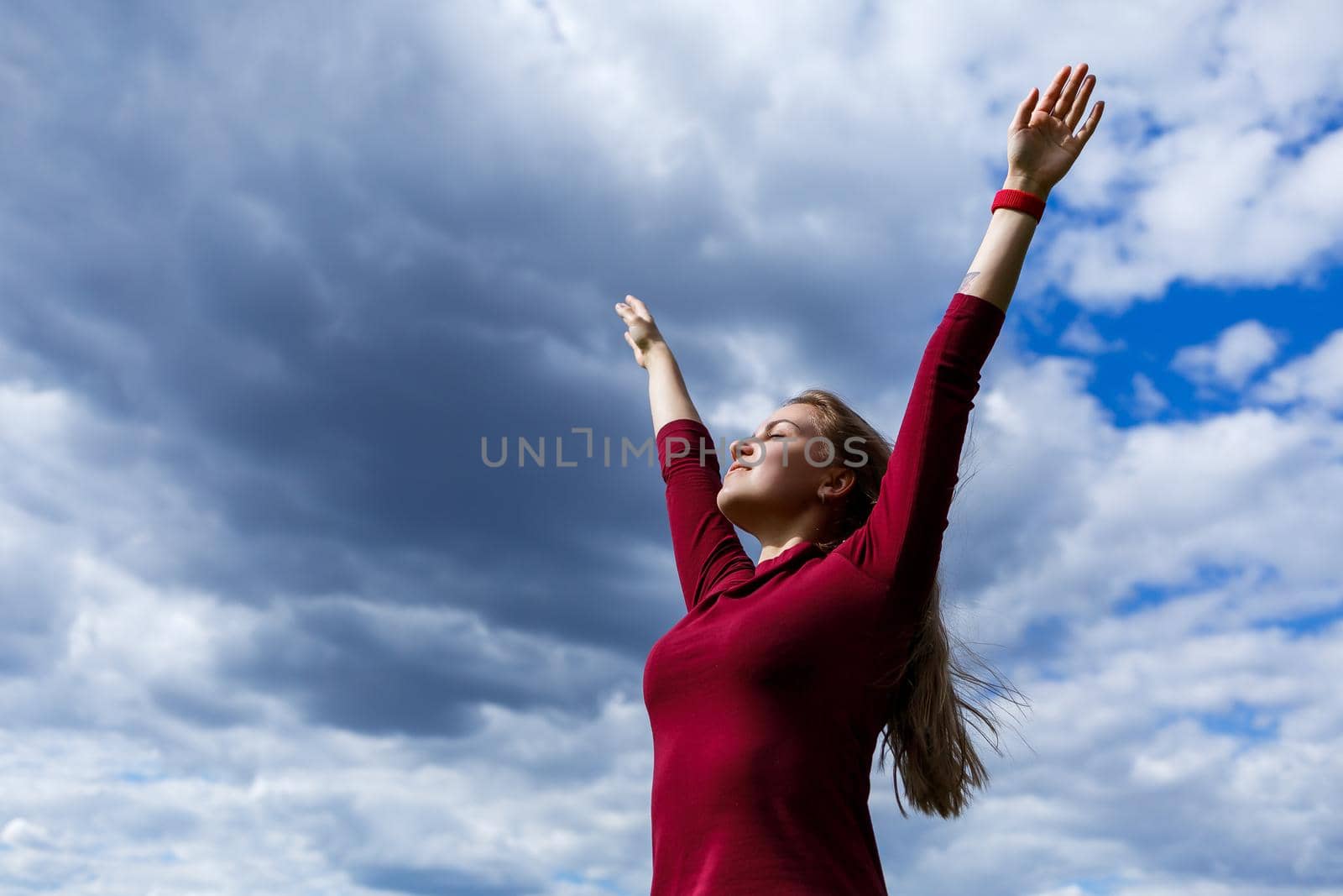 Joyful young girl on a background of the sky with clouds. He raised his hands up and laughed. Happiness in lifestyle. Inspiration in nature. Rest after a good working day.