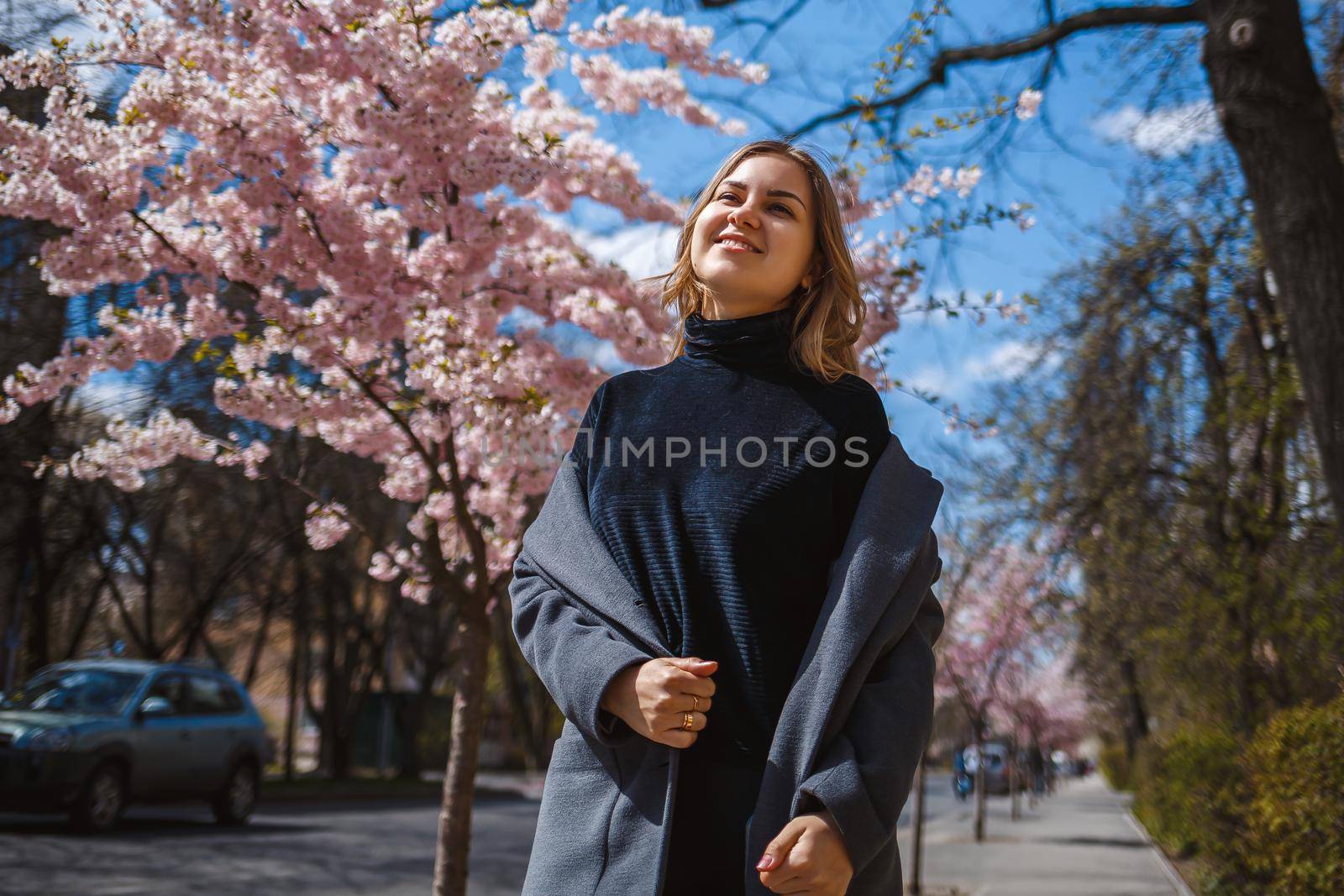 Sakura branches with flowers on a tree on the city streets. Happy woman girl spinning on the street with blooming sakura. Gorgeous fashionable girl outdoors.