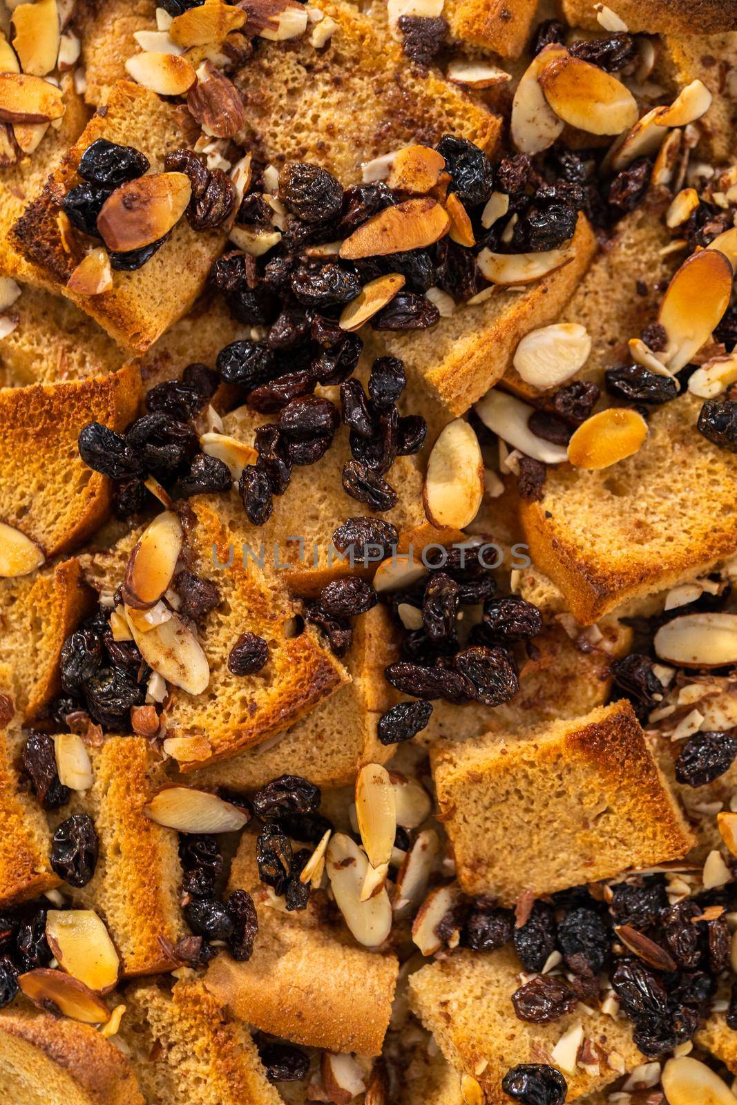 Cooling freshly baked bread pudding with raising and almond slivers in a white casserole dish.