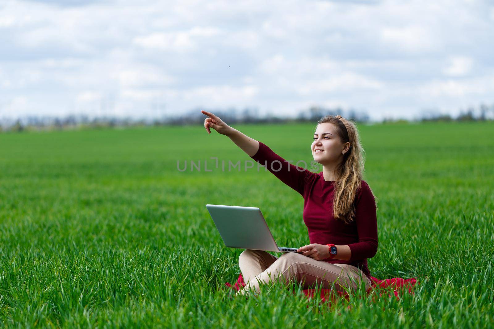 Young successful woman is sitting on green grass with a laptop in her hands. Work on the nature. Student girl working in a secluded place. New business ideas