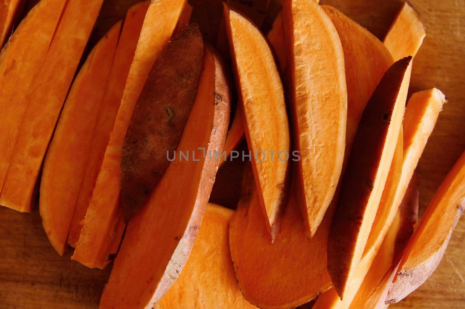 Flat lay composition with cutted wedges of sweet potatoes on wooden table. Copy ad space. Healthy raw vegan food. Banner by artgf