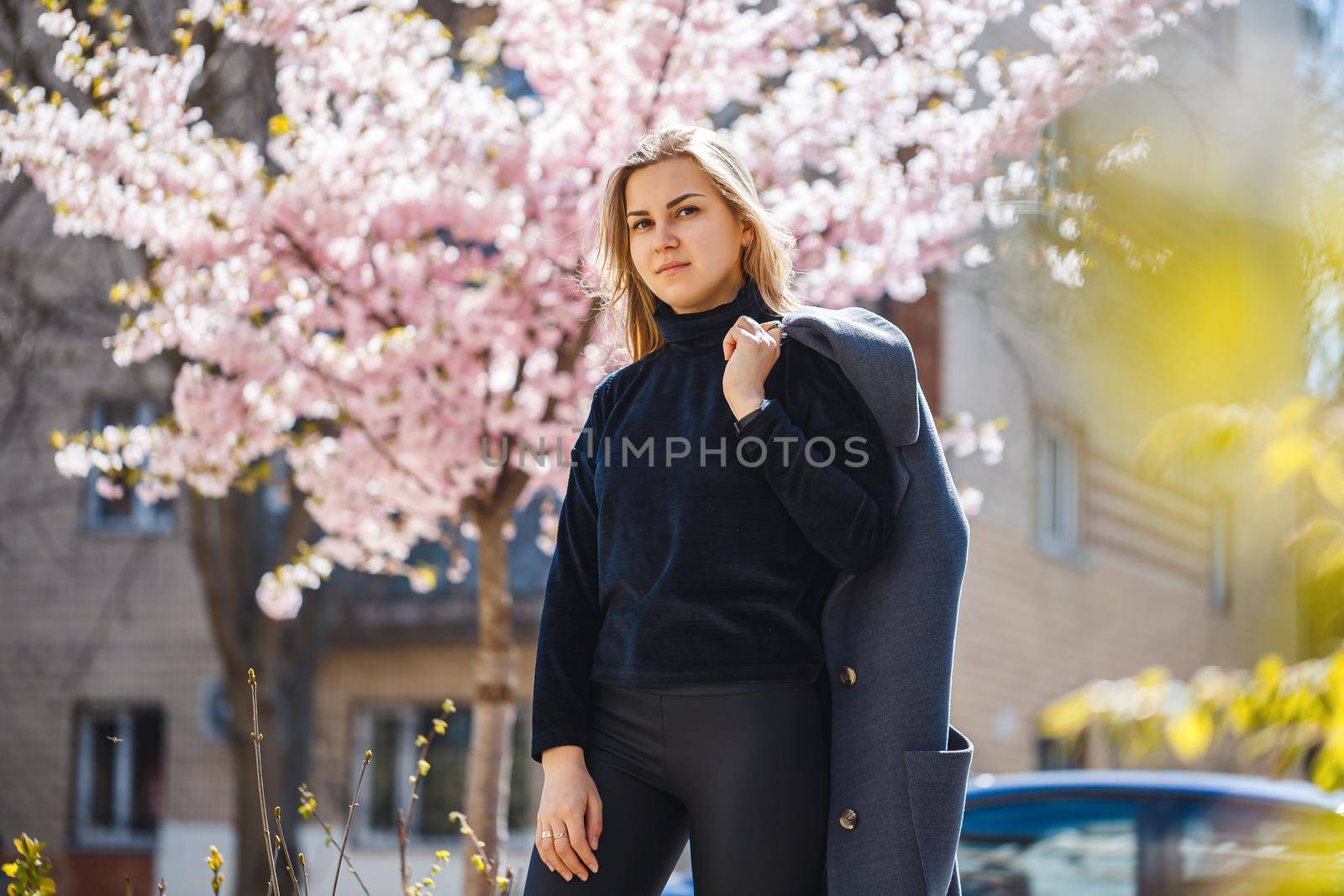 Sakura branches with flowers on a tree on the city streets. Happy woman girl in a gray palette walks along an alley with blooming sakura. Gorgeous fancy girl outdoors. Sakura tree blooming.