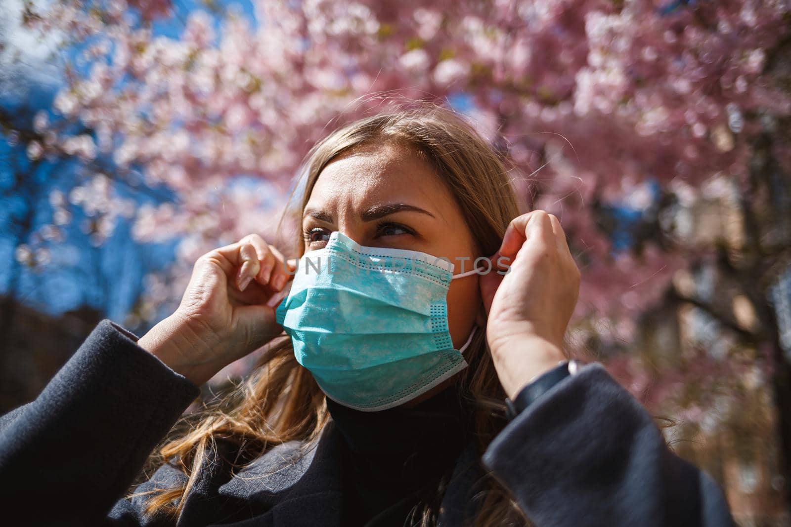 Girl, young woman in a protective sterile medical mask on her face, looking at the camera outdoors, in the spring garden. Air pollution, virus, pandemic coronavirus concept.