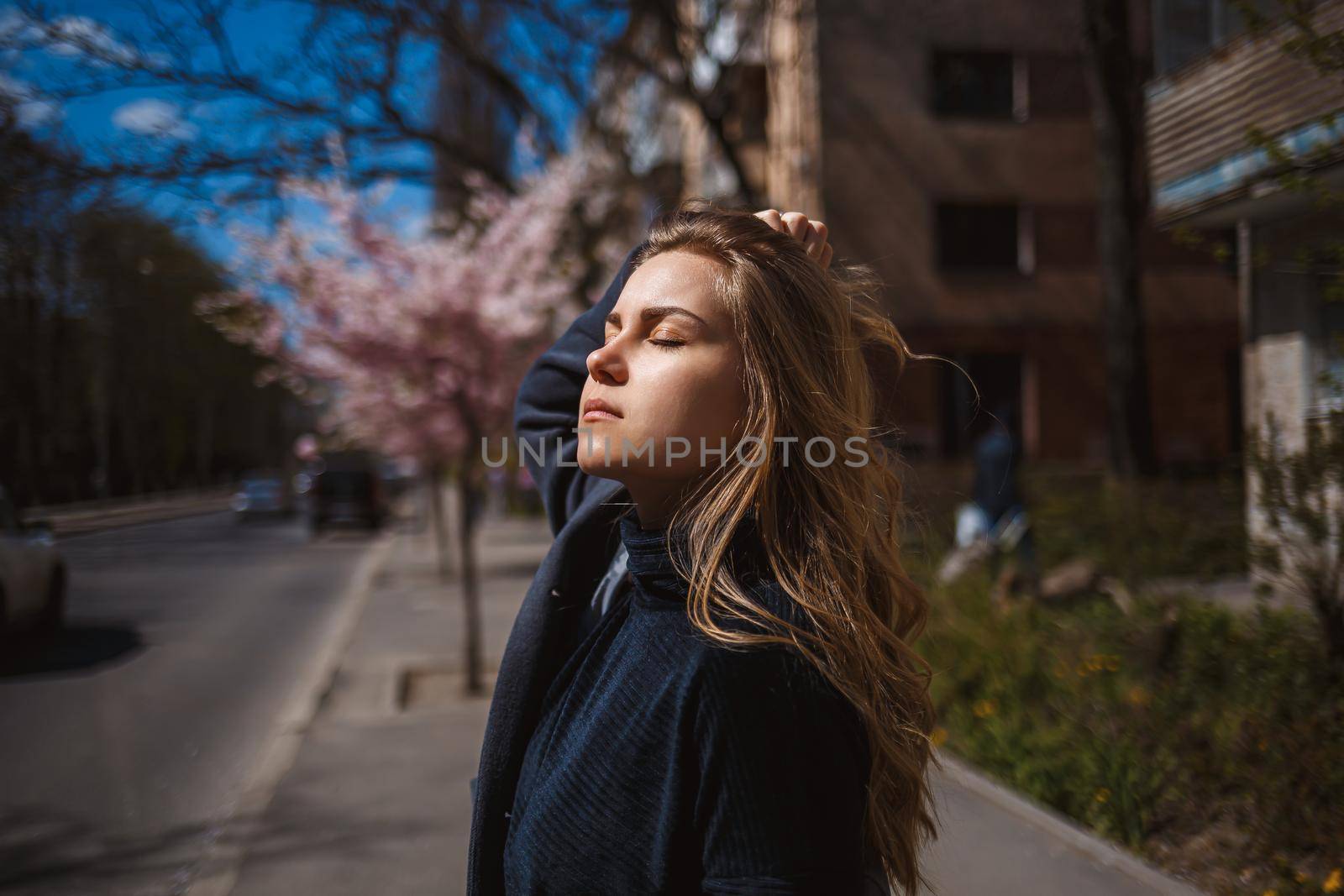 Sakura branches with flowers on a tree on the city streets. Happy woman girl spinning on the street with blooming sakura. Gorgeous fashionable girl outdoors. Sakura tree blossoms.