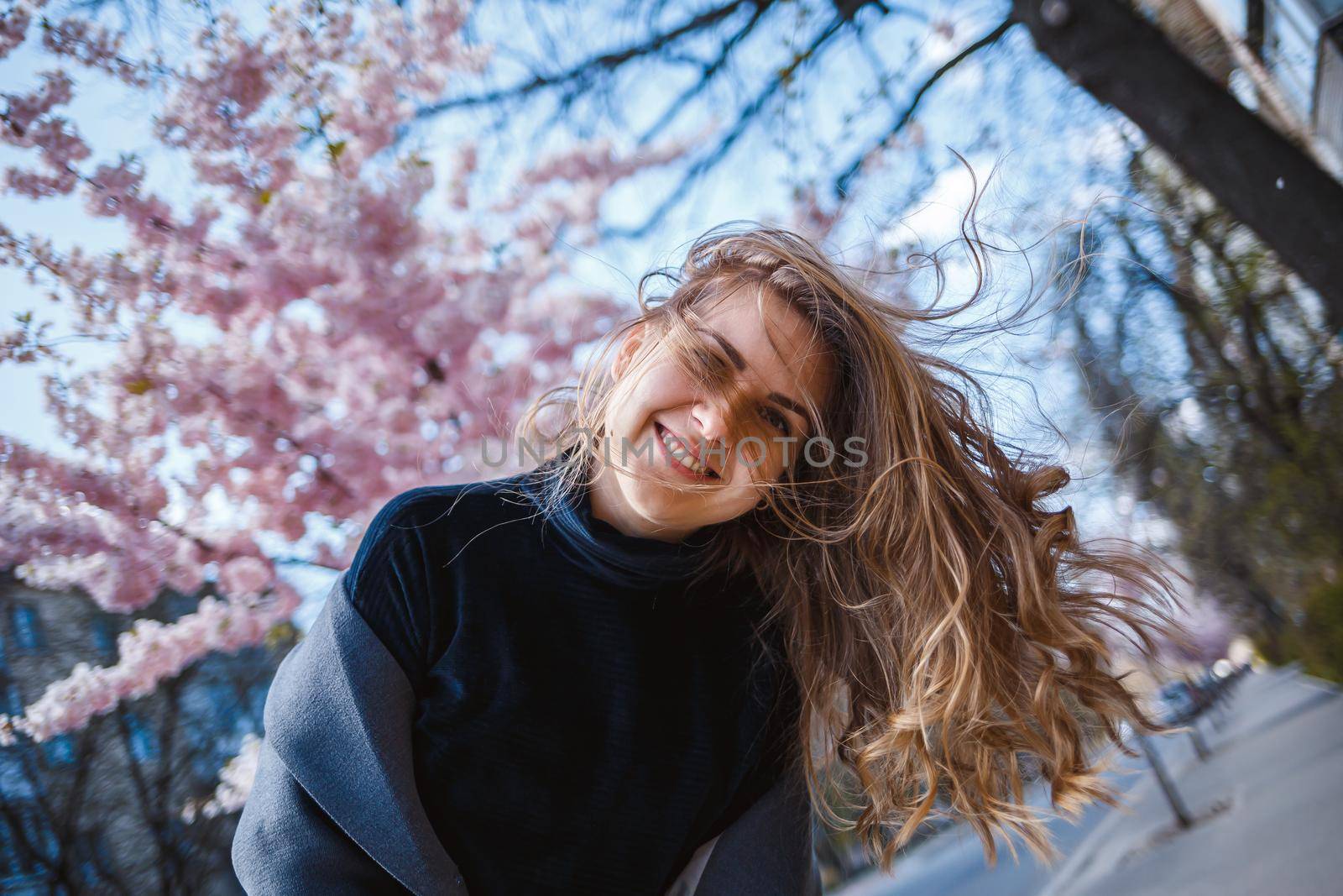 Sakura branches with flowers on a tree on the city streets. Happy woman girl spinning on the street with blooming sakura. Gorgeous fashionable girl outdoors. Sakura tree blossoms.