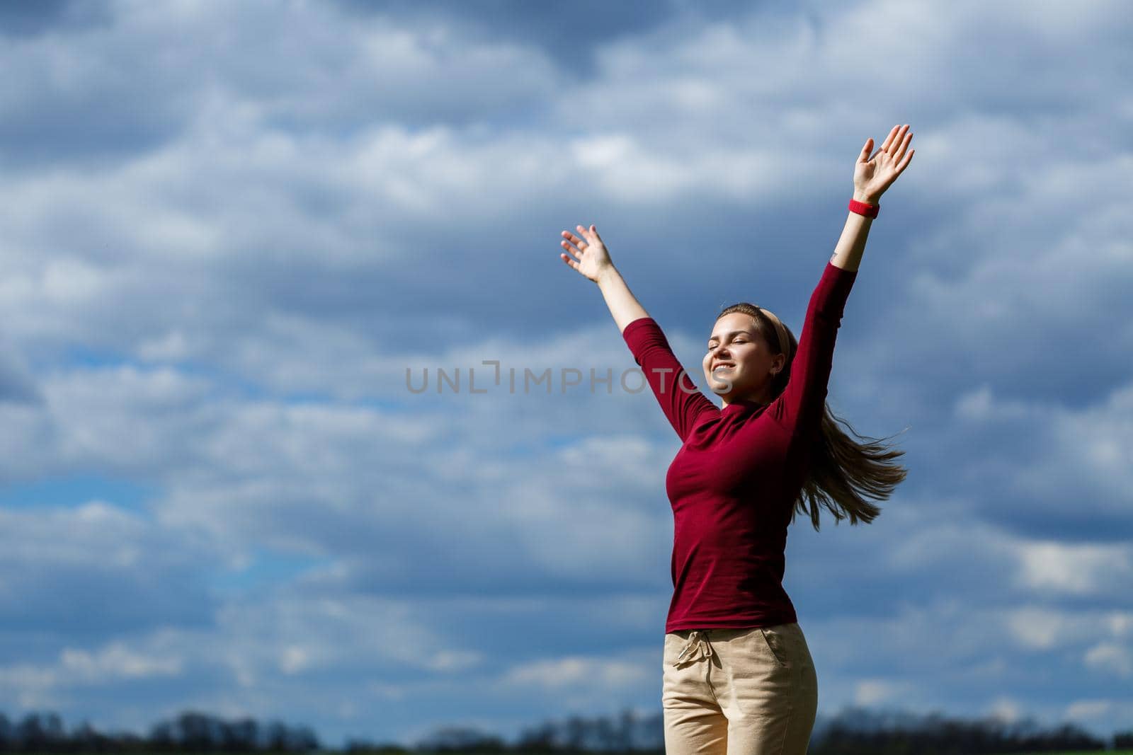 Joyful young girl on a background of the sky with clouds. He raised his hands up and laughed. Happiness in lifestyle. Inspiration in nature. Rest after a good working day.