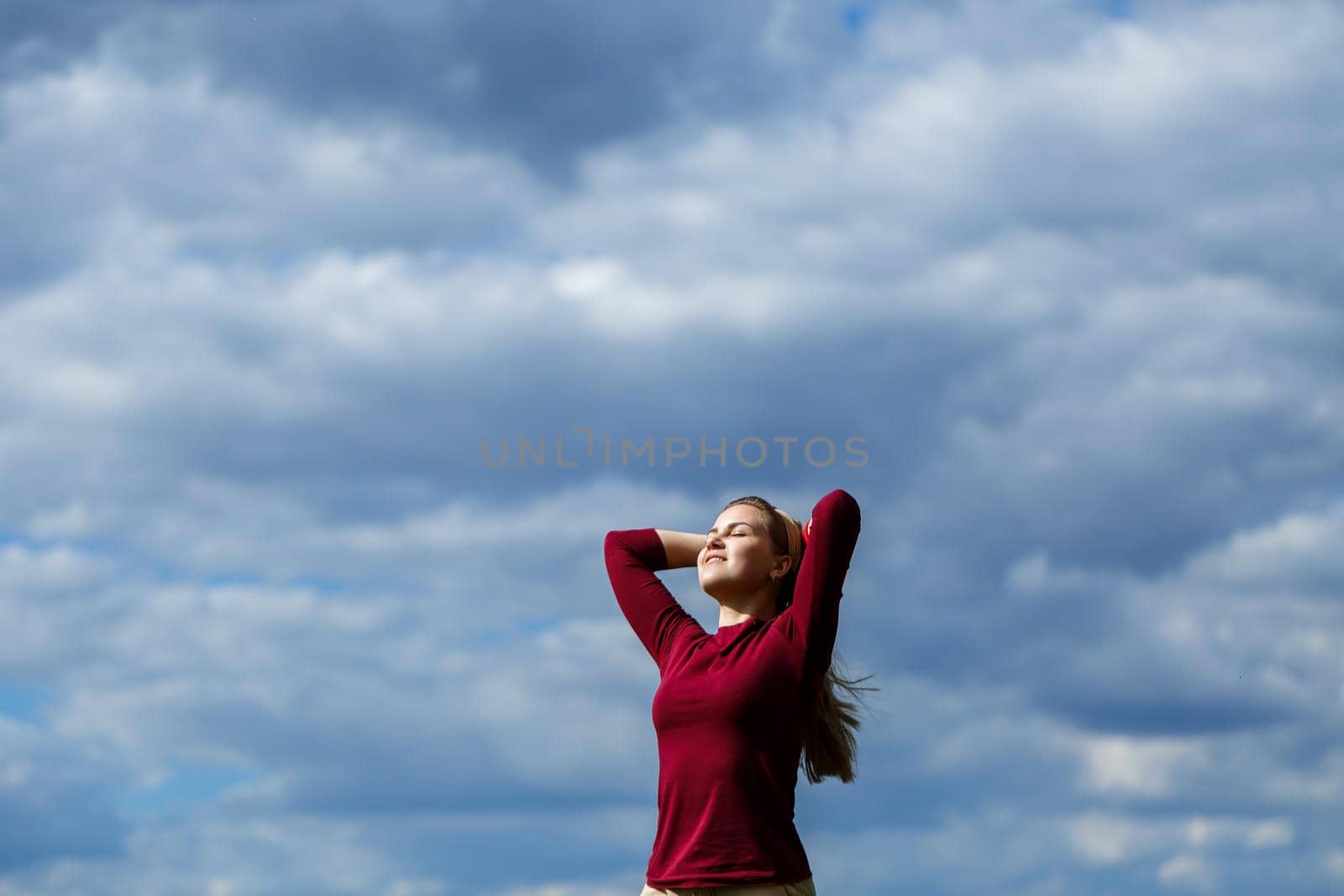 Joyful young girl on a background of the sky with clouds. He raised his hands up and laughed. Happiness in lifestyle. Inspiration in nature. Rest after a good working day.