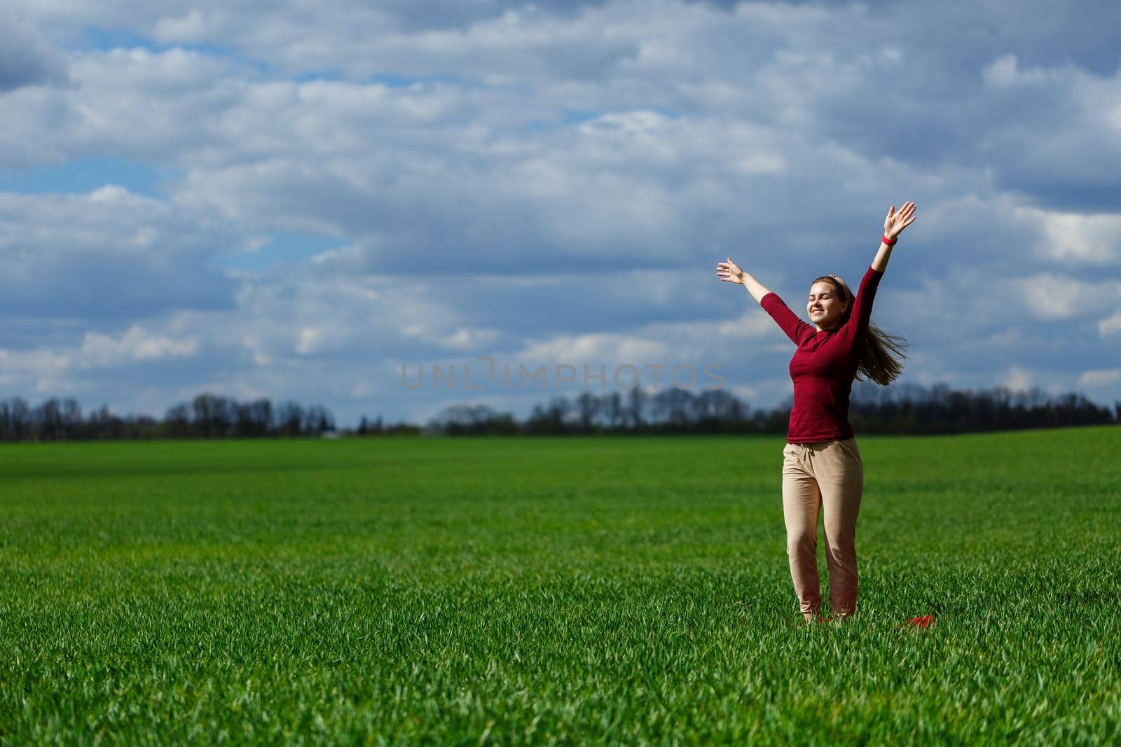 Beautiful young blonde woman stands on green grass in a park. Blue sky with clouds. The girl smiles and enjoys a good day.