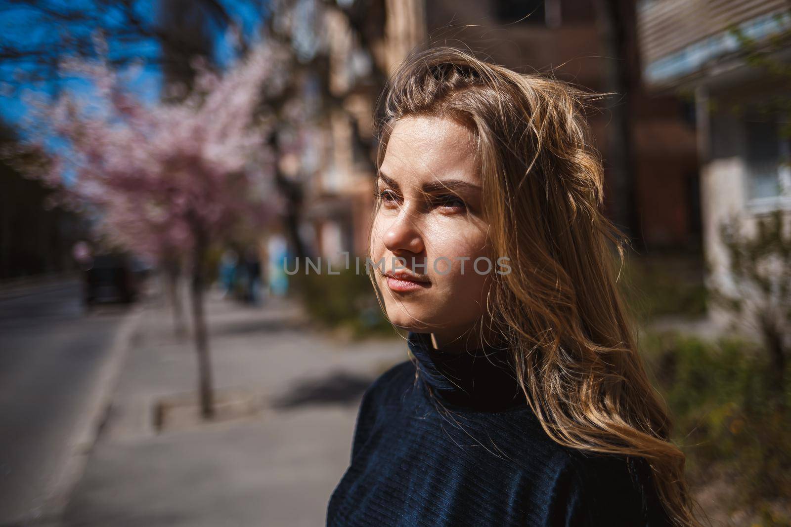 Sakura branches with flowers on a tree on the city streets. Happy woman girl spinning on the street with blooming sakura. Gorgeous fashionable girl outdoors. Sakura tree blossoms.